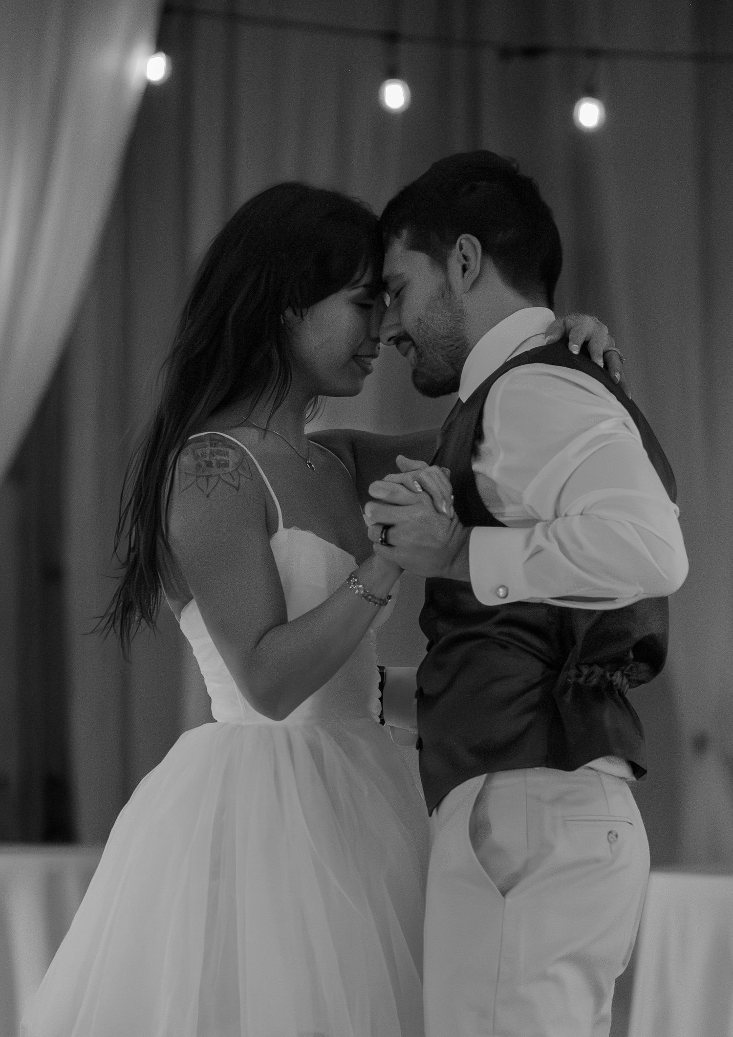 Black and white photo of a bride and groom sharing their first dance at a wedding reception.
