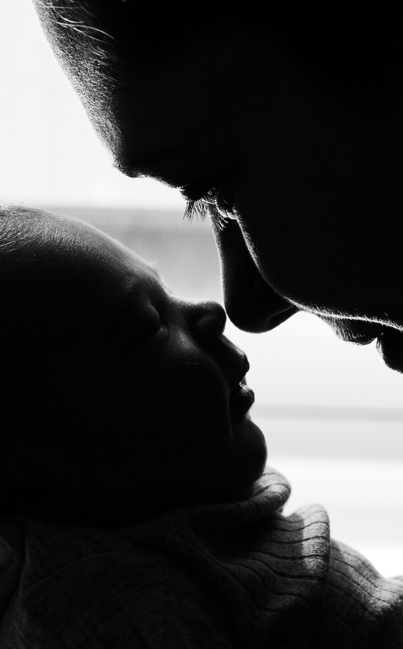 Black and white close-up of a bearded father gently kissing his newborn baby in a tender moment.