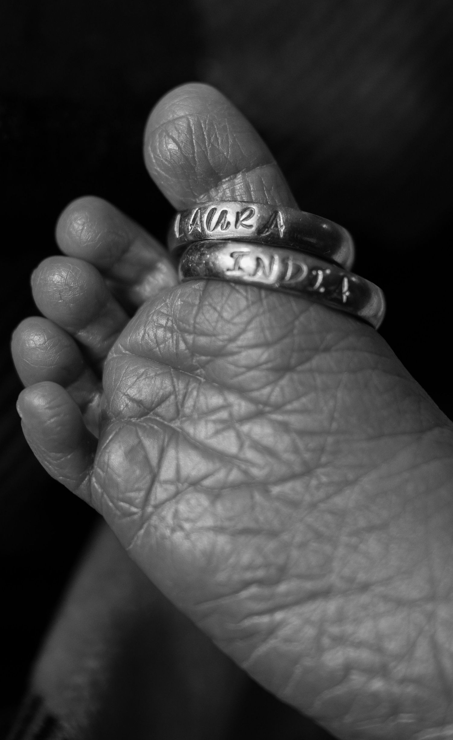 Black and white close-up of a newborn baby foot with two silver rings on the big toe.
