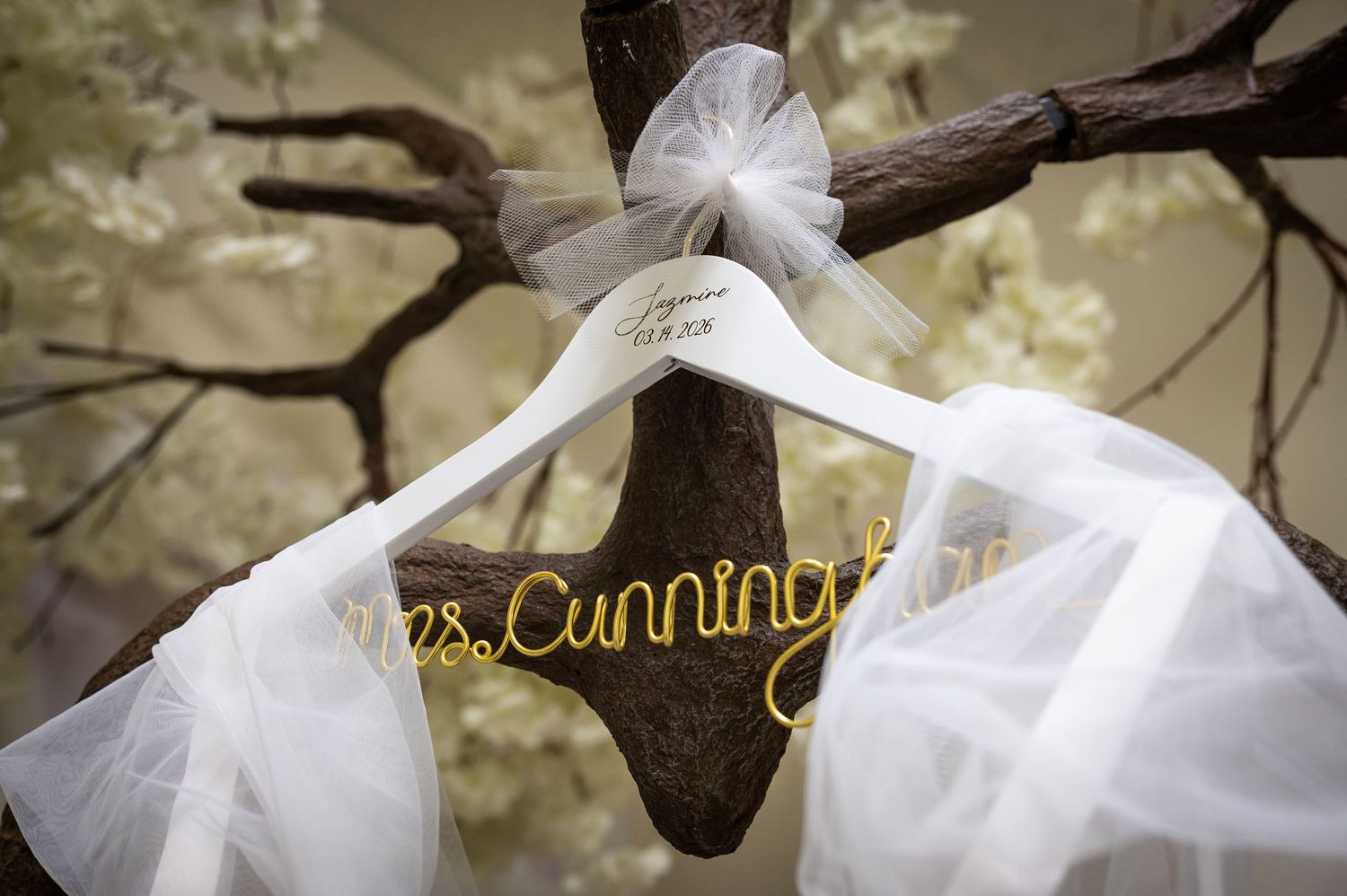 White wedding dress hanger personalized with Mrs. Cunningham in gold wire, displayed on rustic tree branch with tulle.