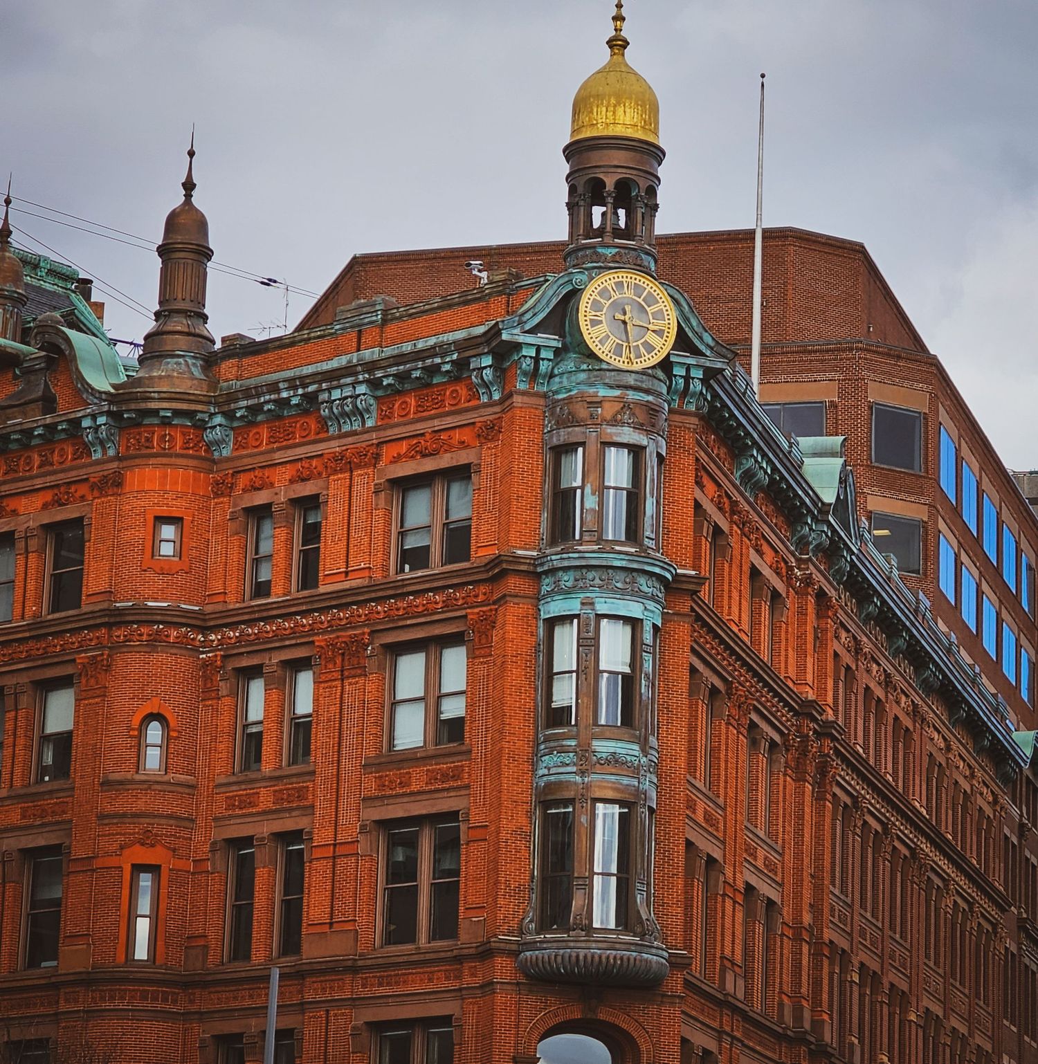 Historic red brick building with gold dome, clock tower, and green copper accents under cloudy skies.