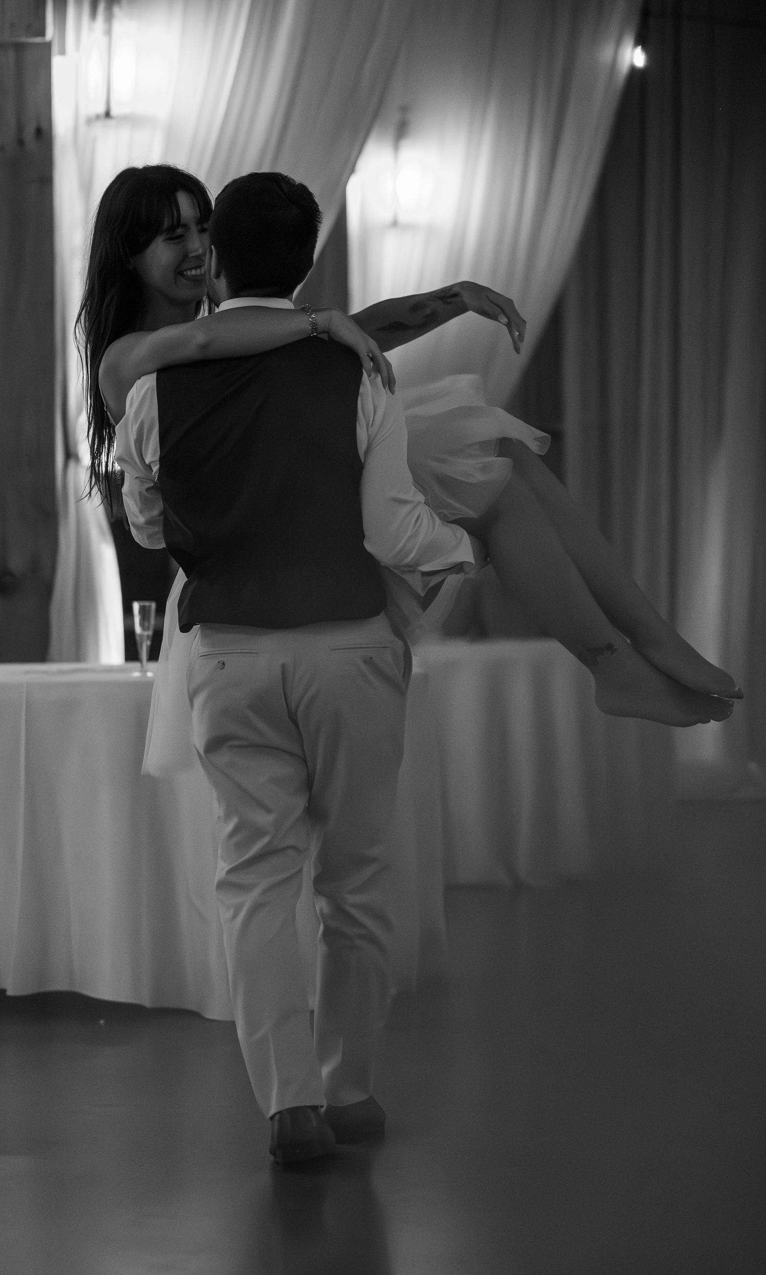 Black and white photo of a groom lifting his smiling bride during a romantic wedding reception dance.