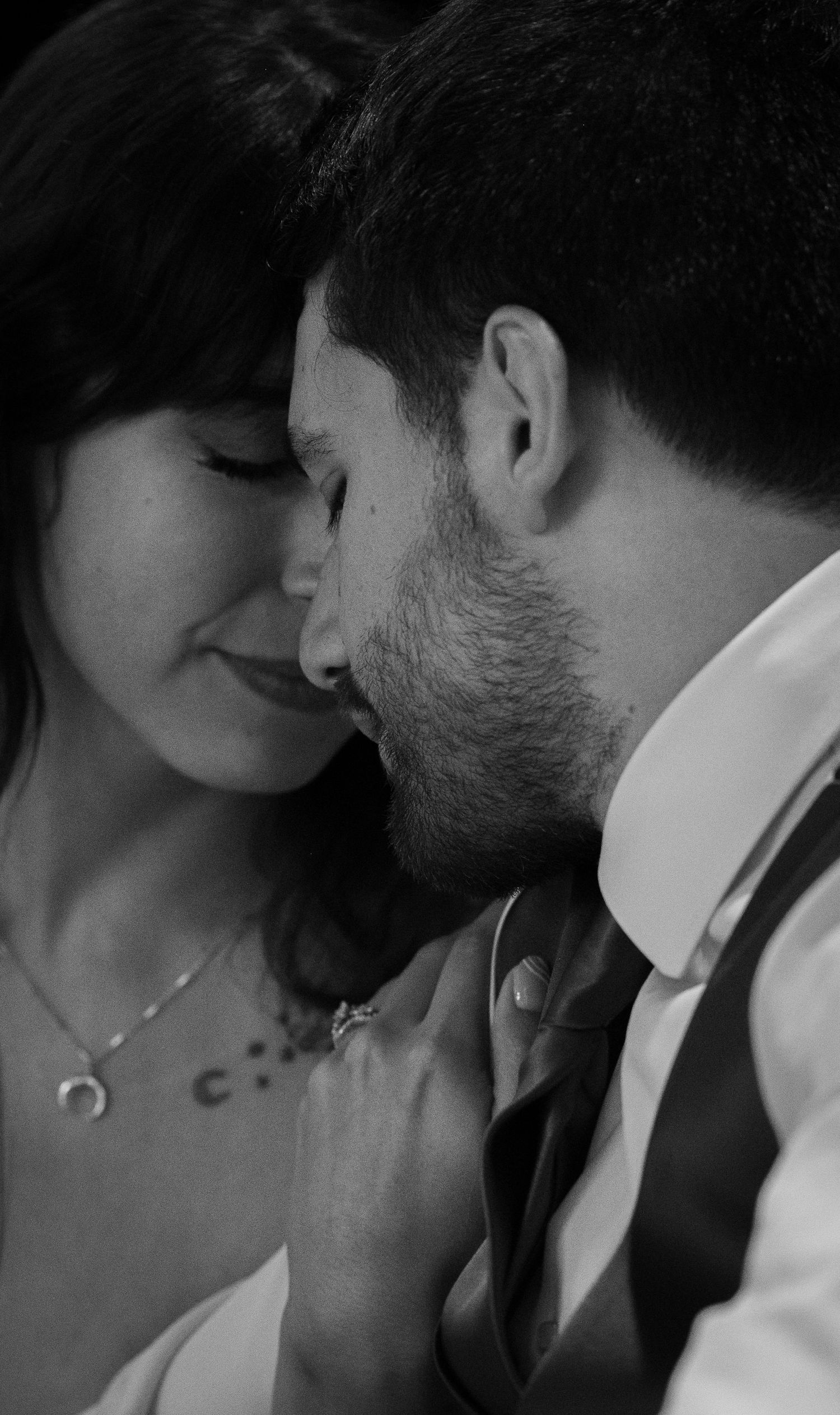 Black and white photo of a couple sharing an intimate moment, the man gently kissing the smiling woman's cheek.