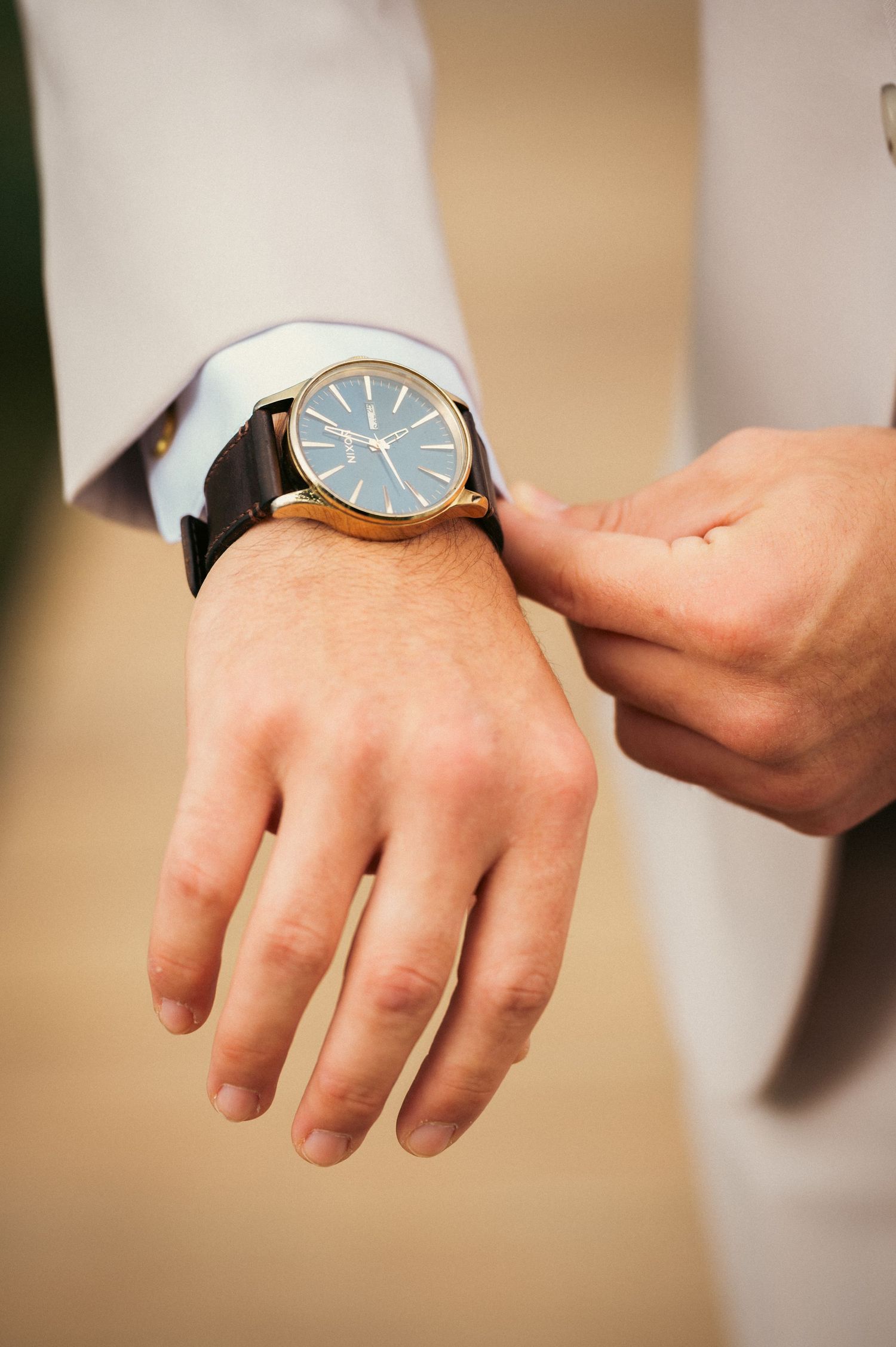 Close-up of groom adjusting gold watch with blue face on his wrist.