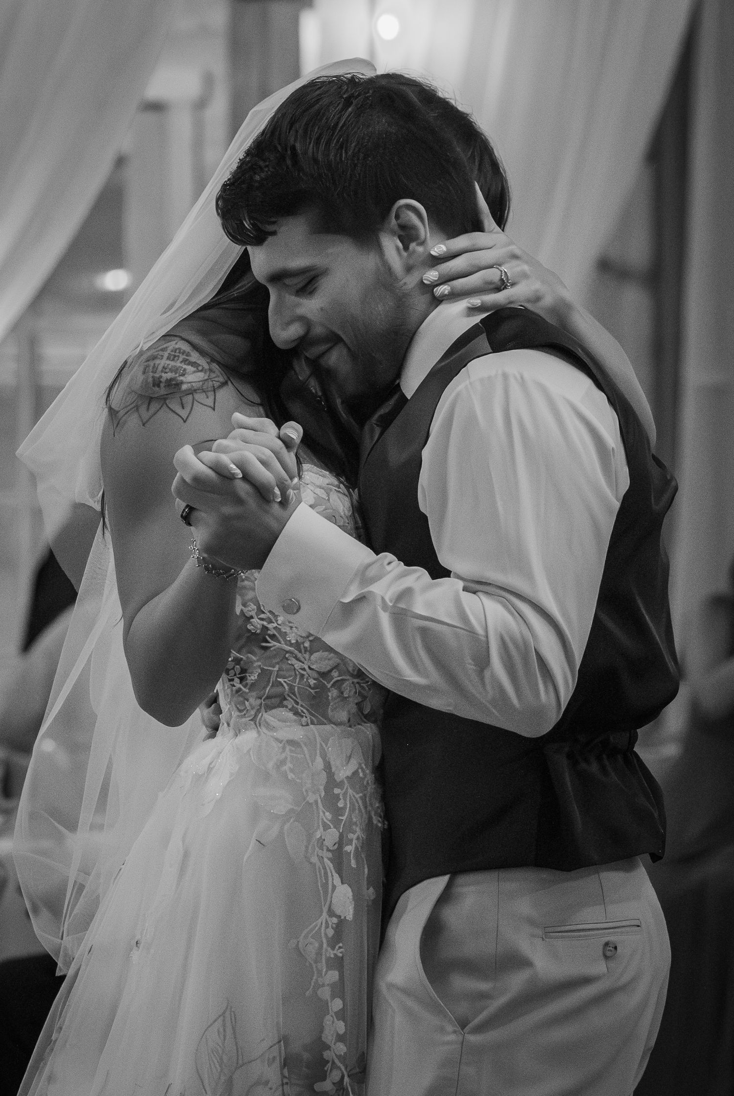 Black and white photo of a bride and groom sharing their first dance, embracing closely at their wedding reception.