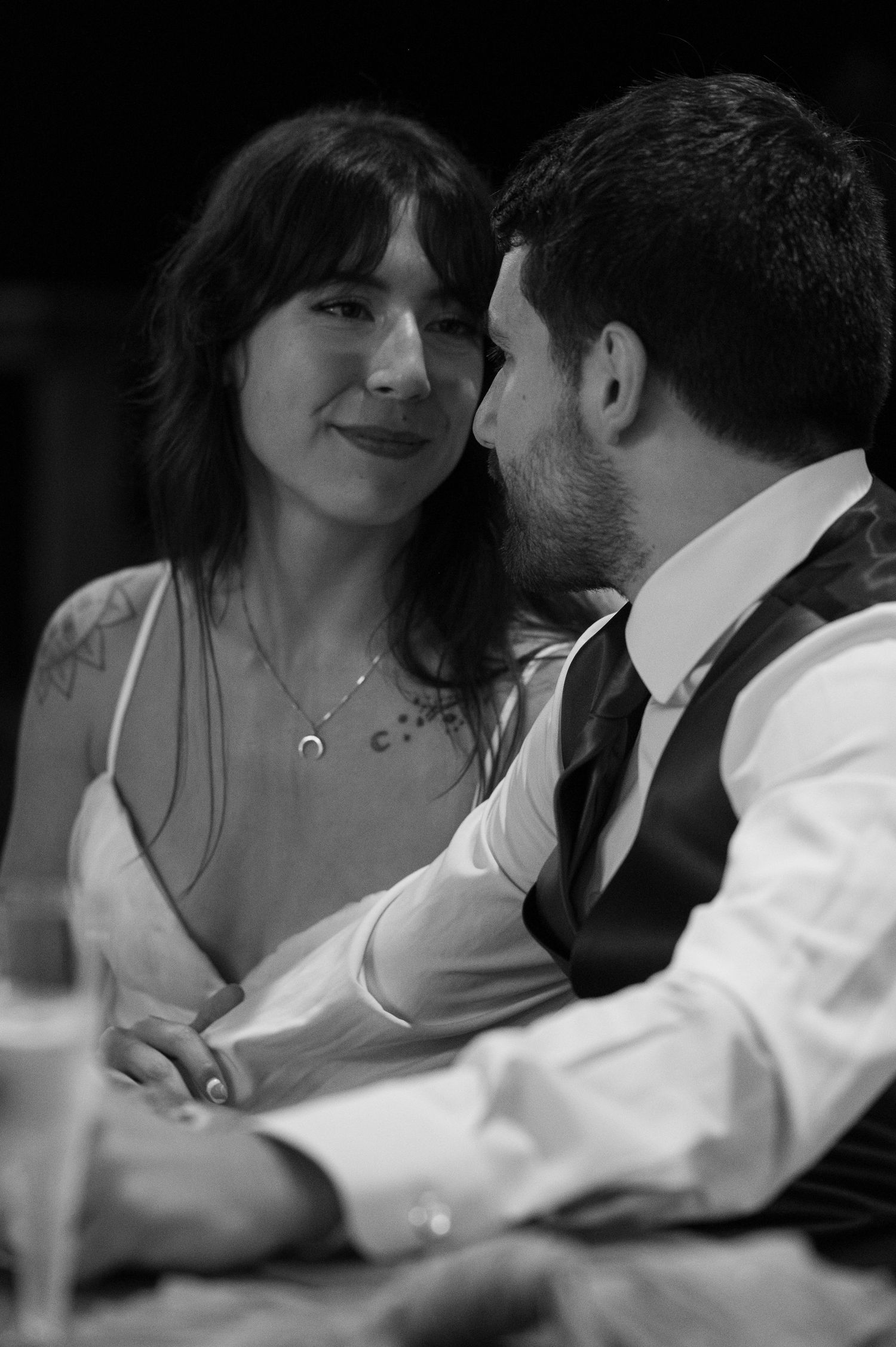 Black and white photo of a couple sharing an intimate moment, woman smiling warmly at bearded man in vest and tie.