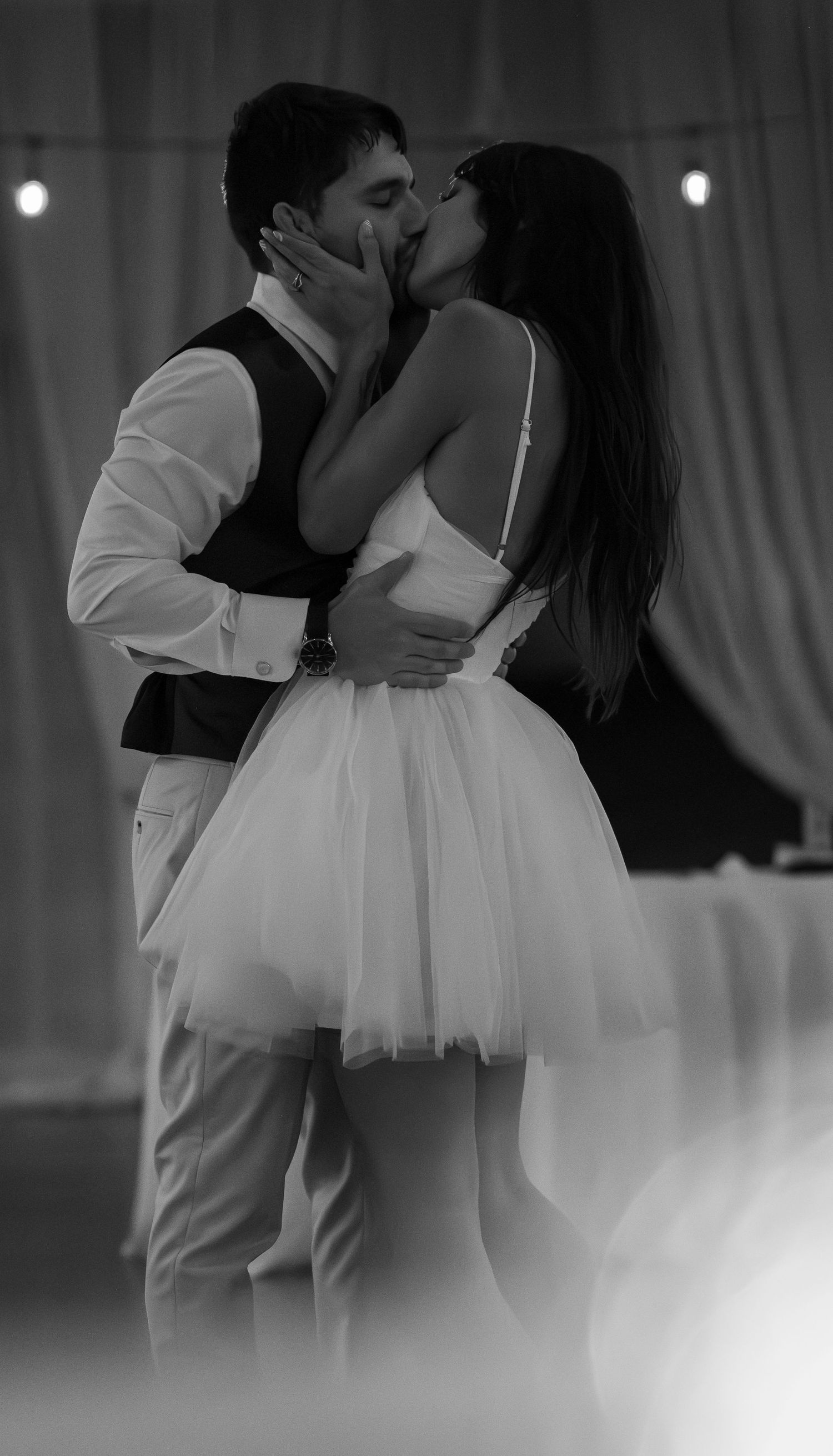 Black and white photo of a couple sharing a romantic kiss on their wedding day, bride in short tulle dress.