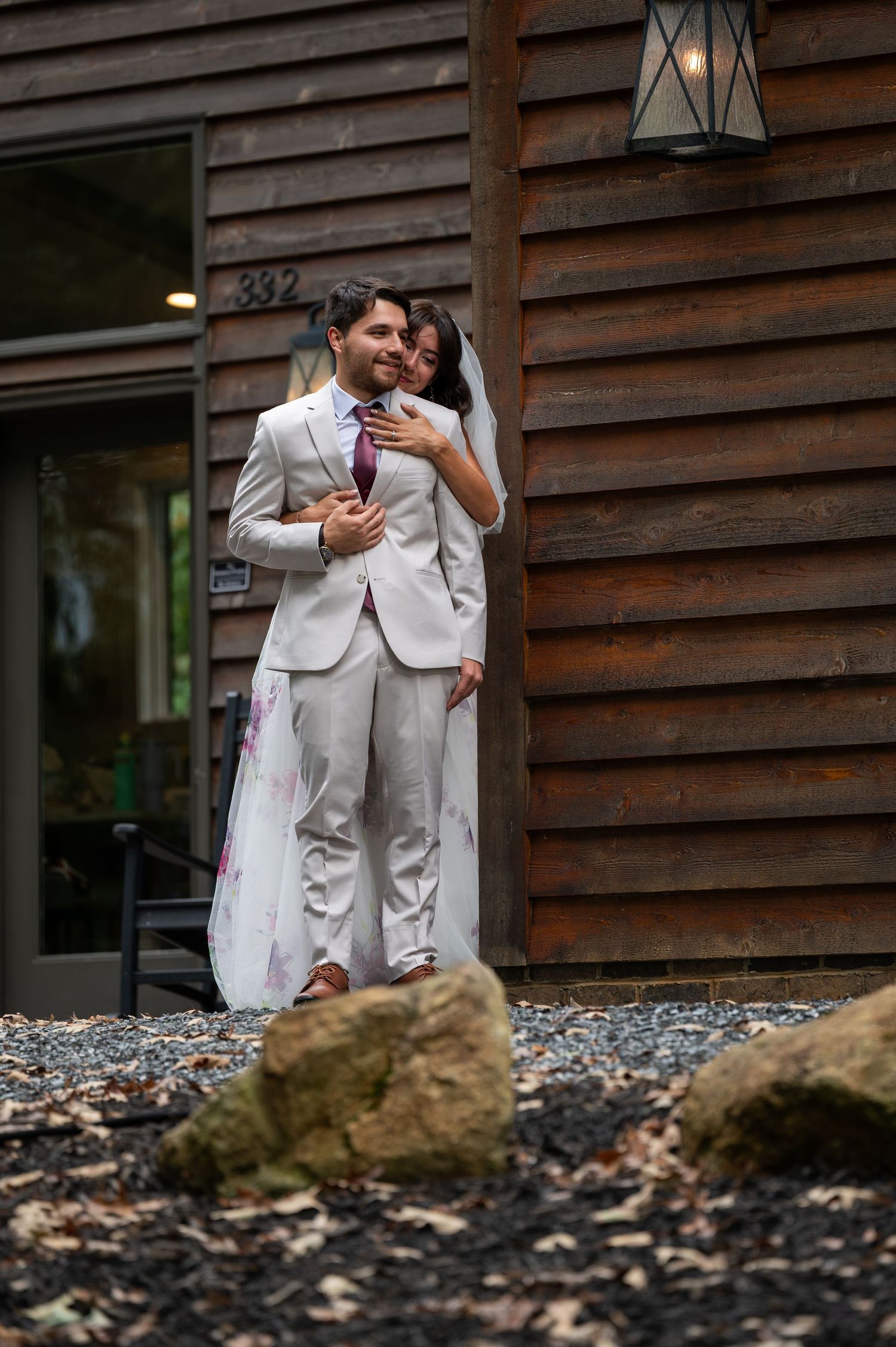 Bride and groom embracing outside rustic wooden cabin with address number 332.