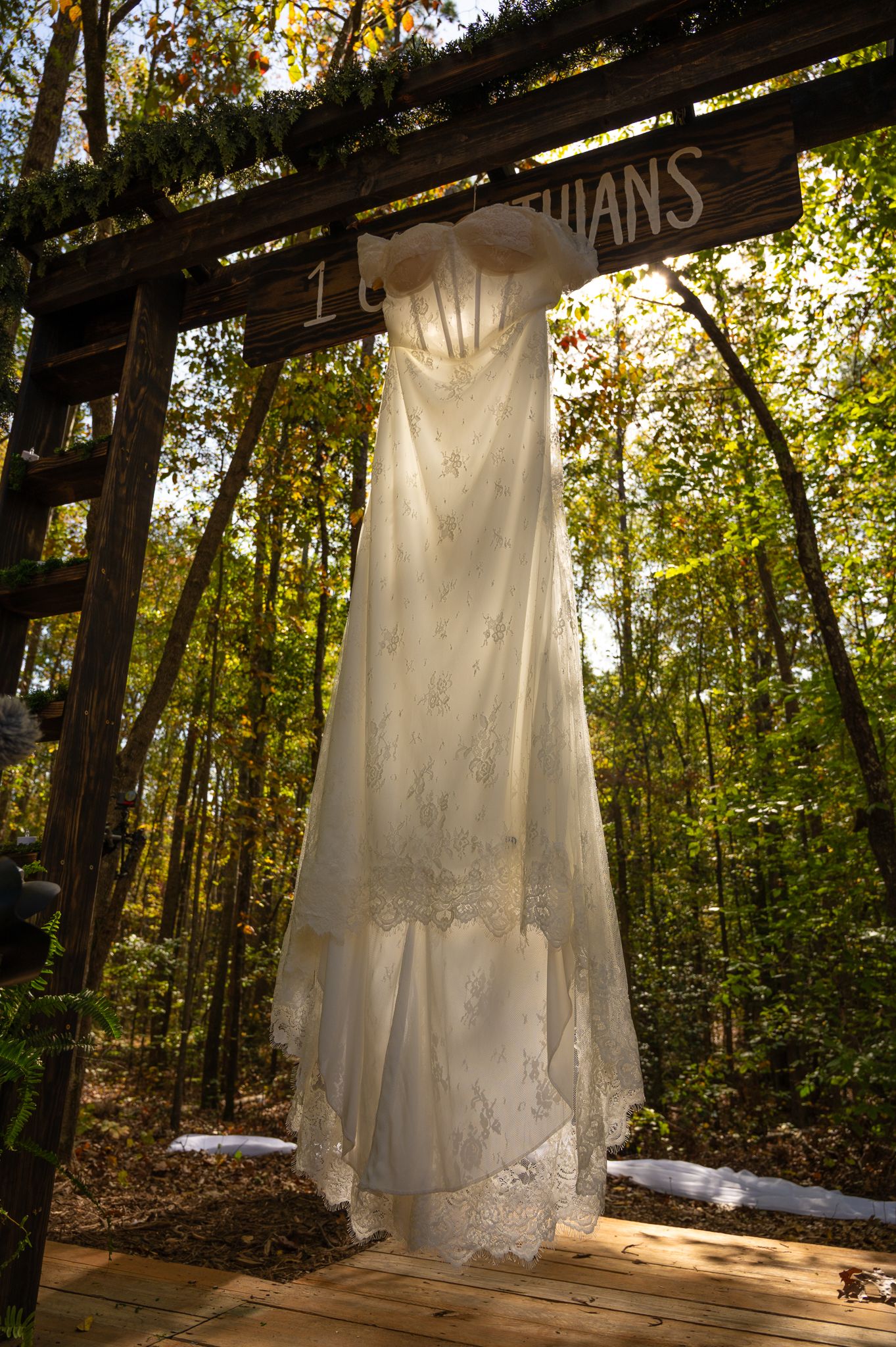 Elegant white lace wedding dress hanging on a rustic wooden arch in a forest setting.
