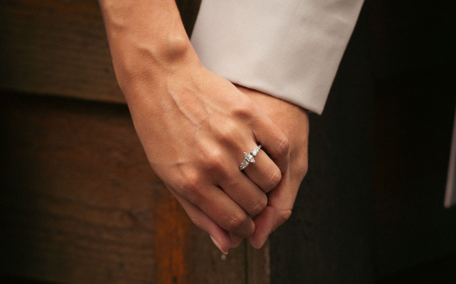 Close-up of bride and groom holding hands showing diamond engagement and wedding rings.