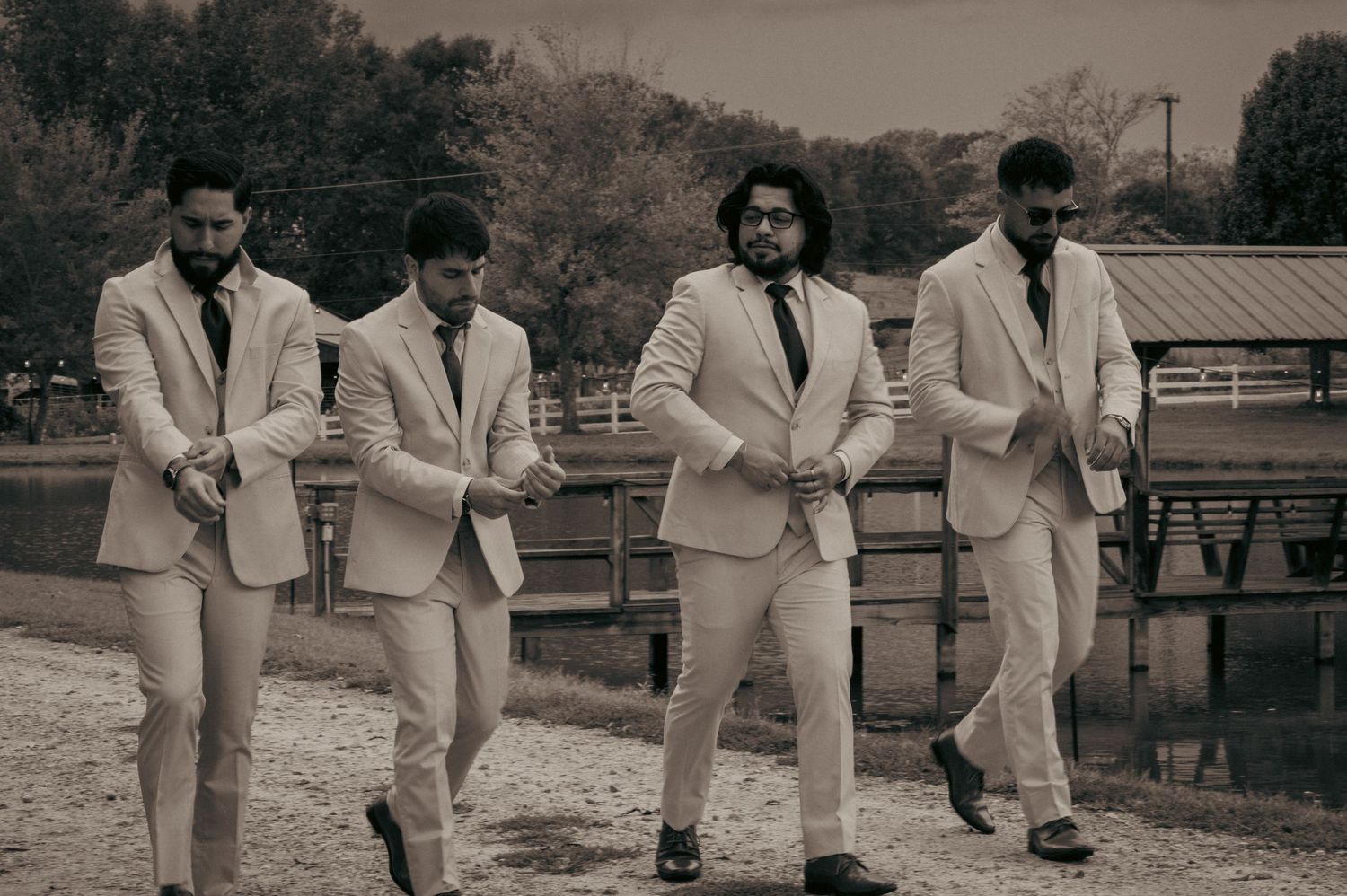 Four men in white suits walk confidently in black and white outdoor photo.