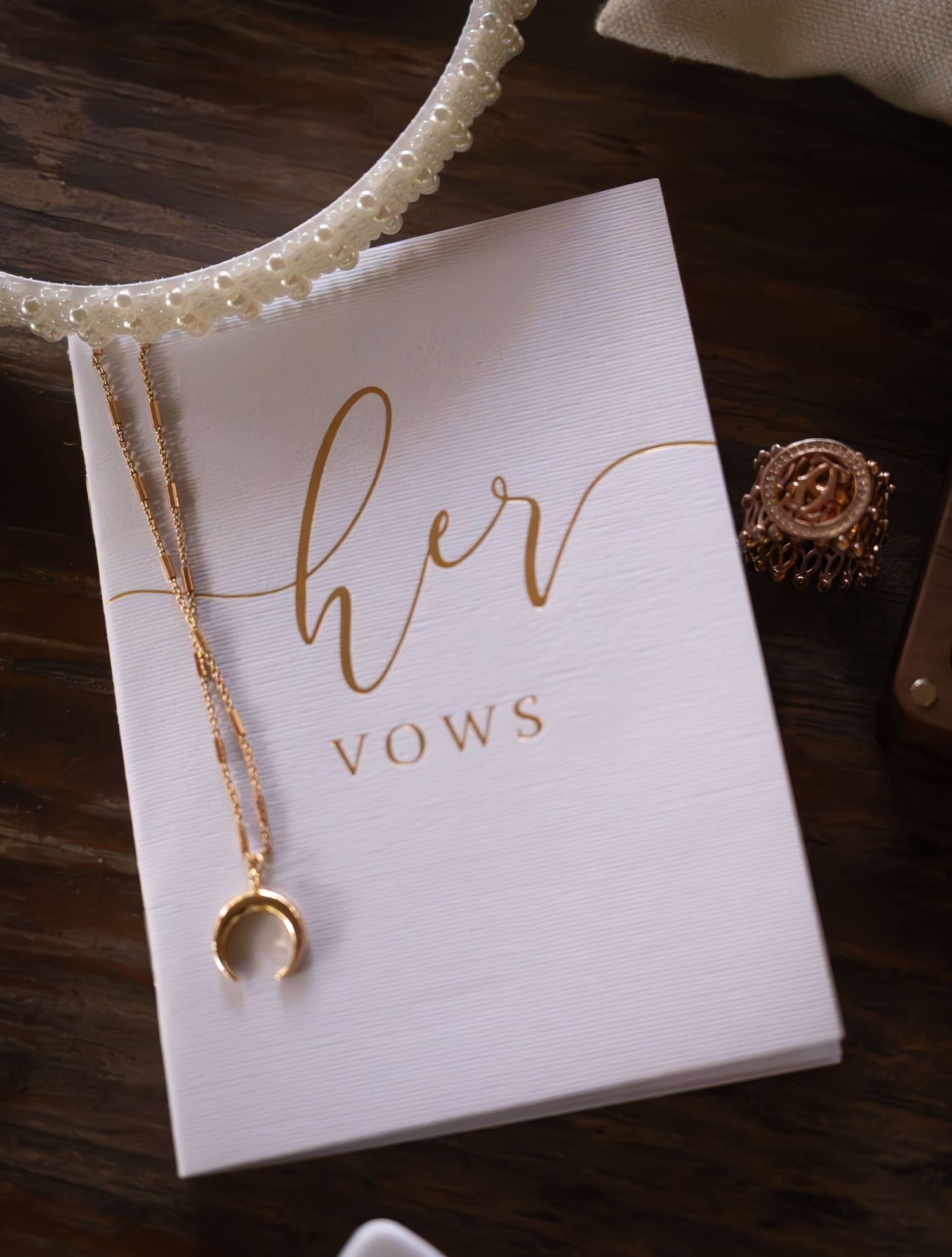 Elegant white vow book with gold script reading her vows, adorned with a crescent moon necklace and ring.