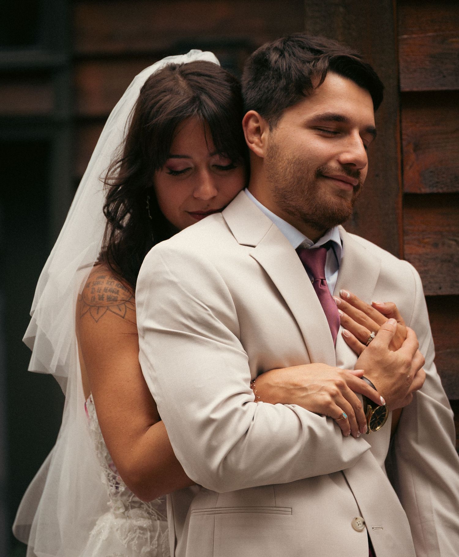 A bride in a white veil embraces a groom in a beige suit, sharing a tender moment on their wedding day.
