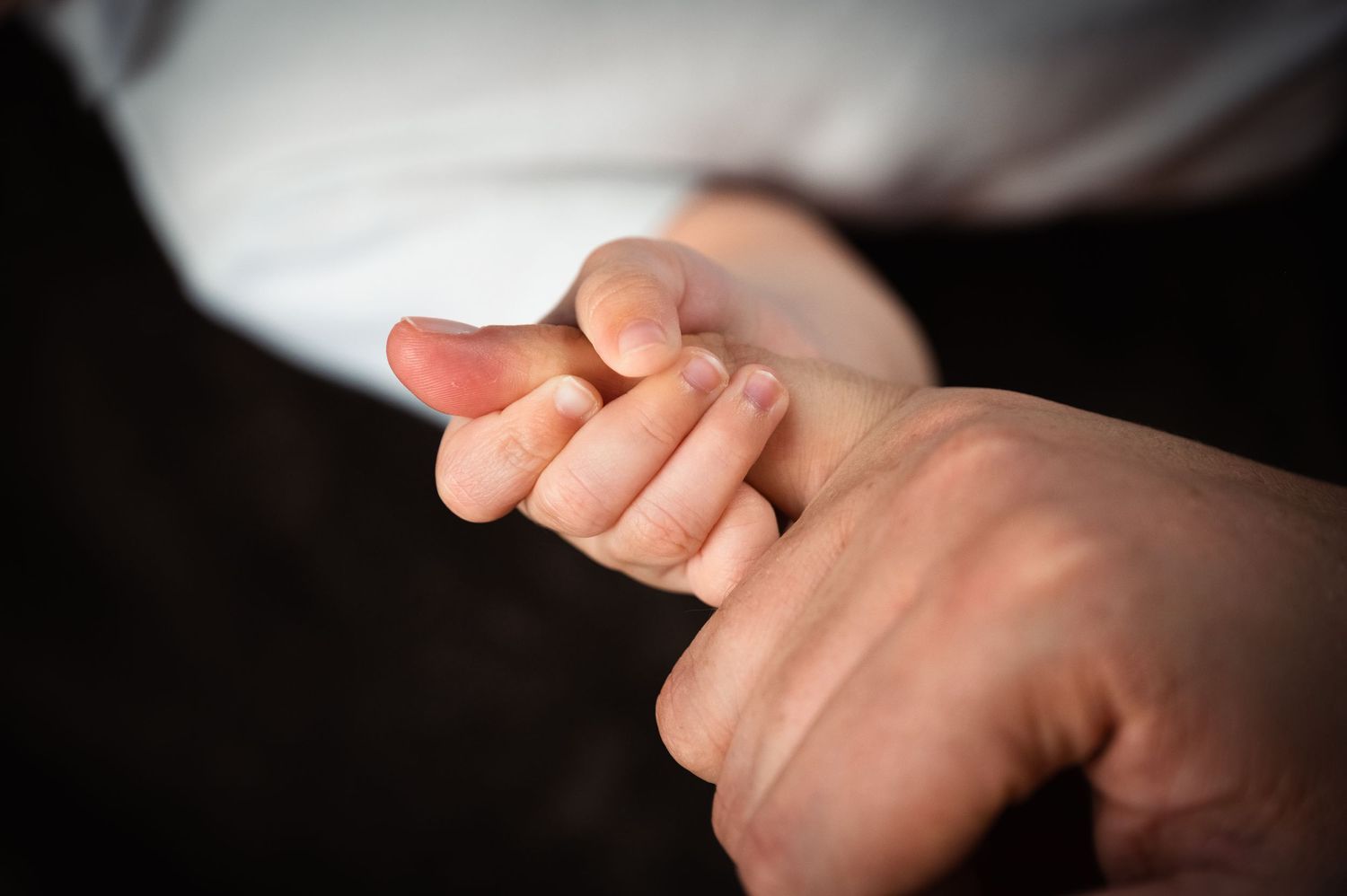 A newborn baby's tiny hand gently gripping an adult's finger, symbolizing love and new parenthood.