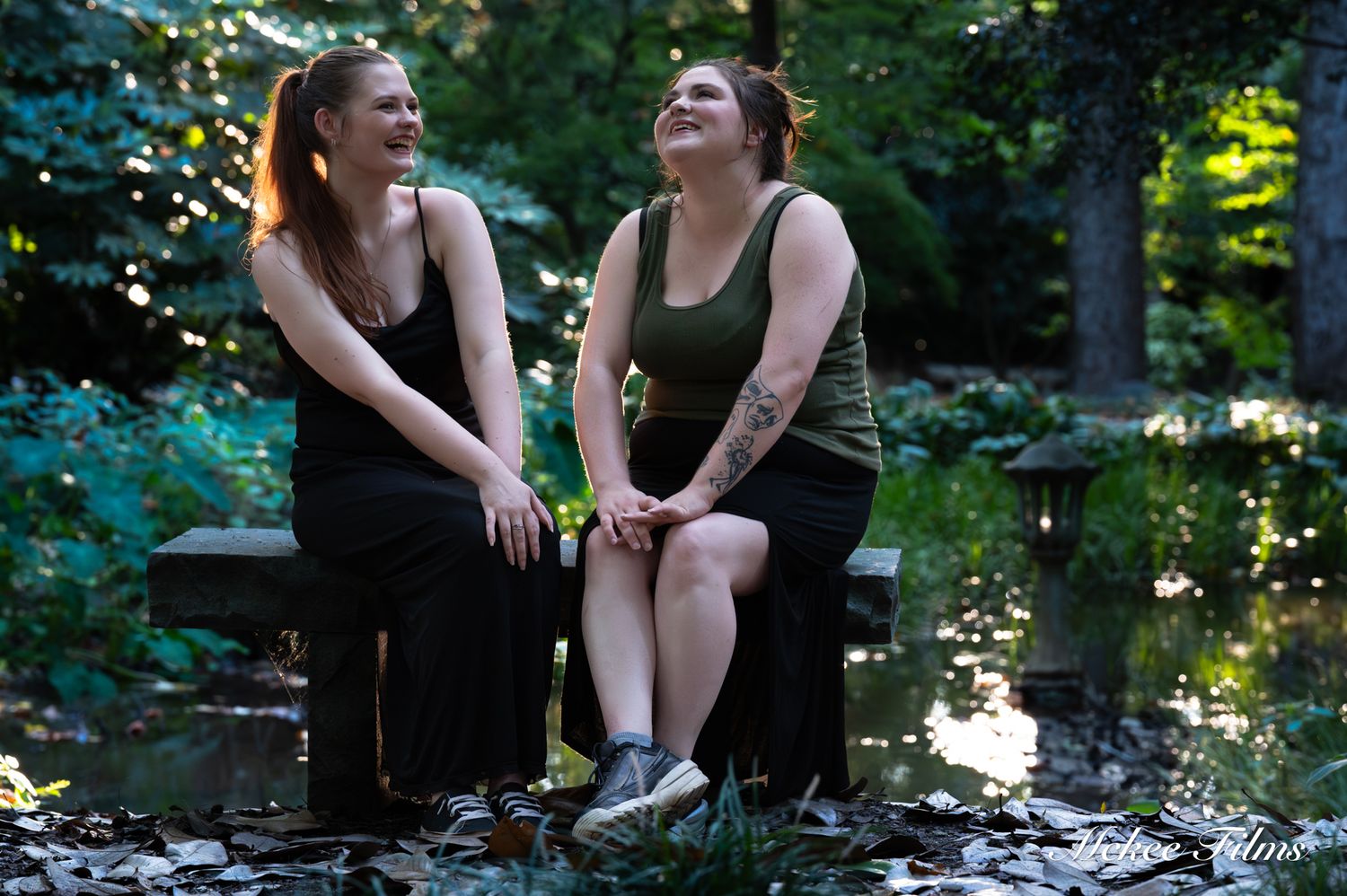 Two women laughing together on a bench in a lush green garden setting.