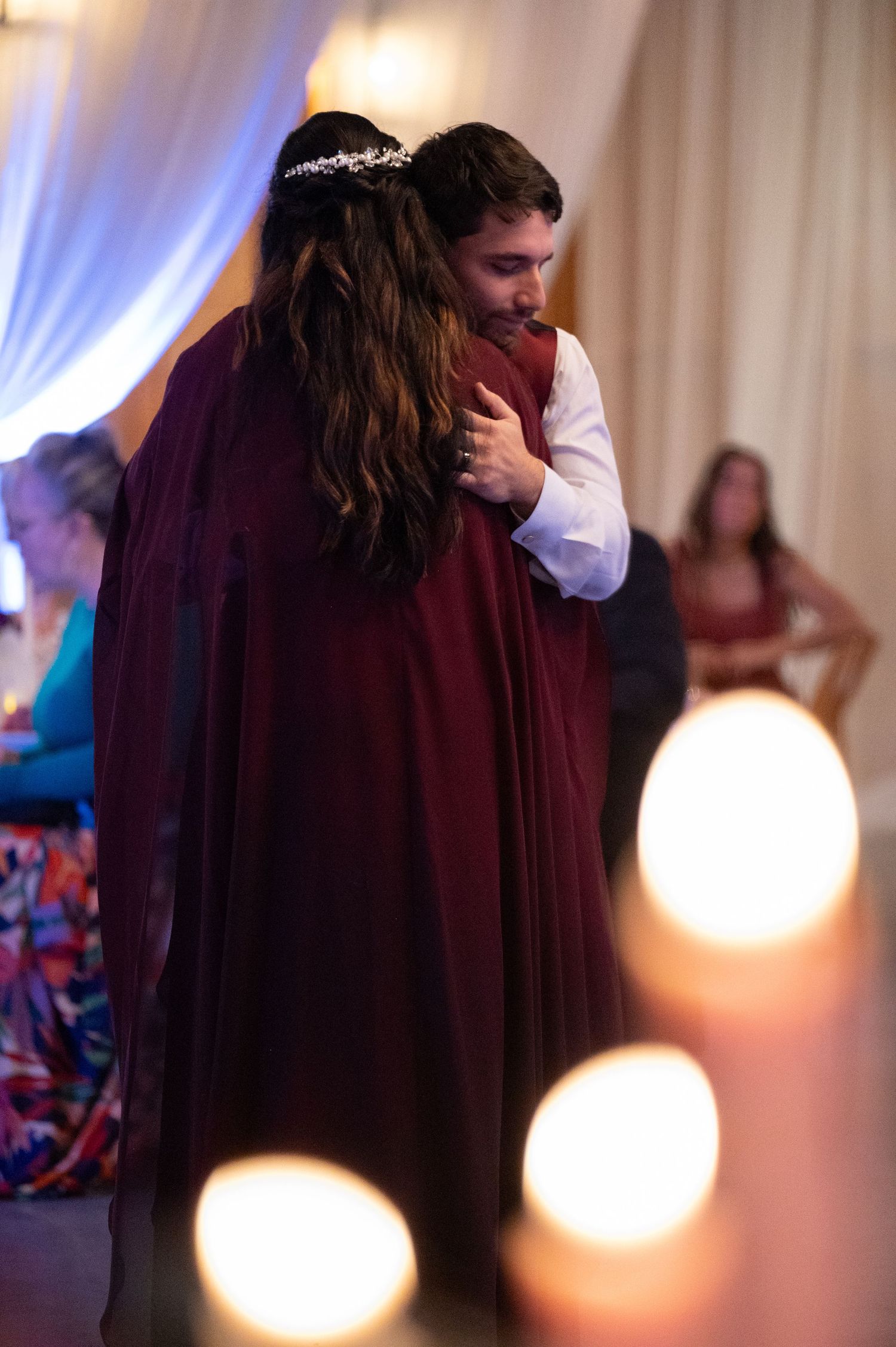 Couple sharing a romantic dance in burgundy wedding attire surrounded by glowing candles.