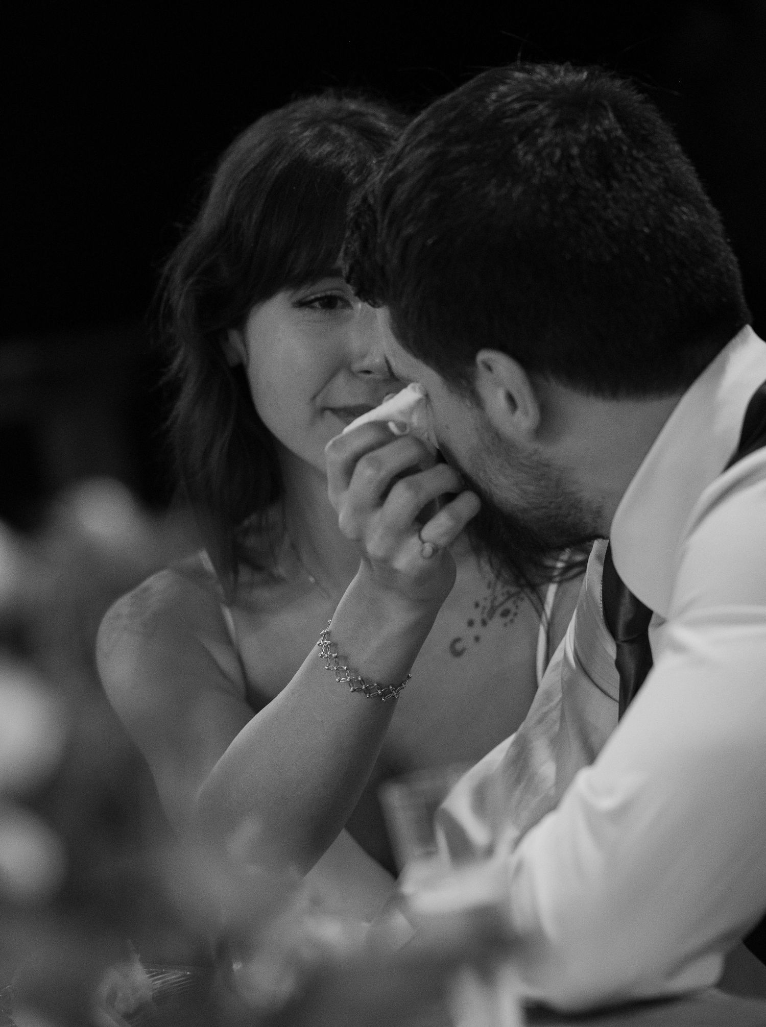 Black and white wedding photo of groom kissing bride's hand as she wipes tears, capturing an emotional moment.