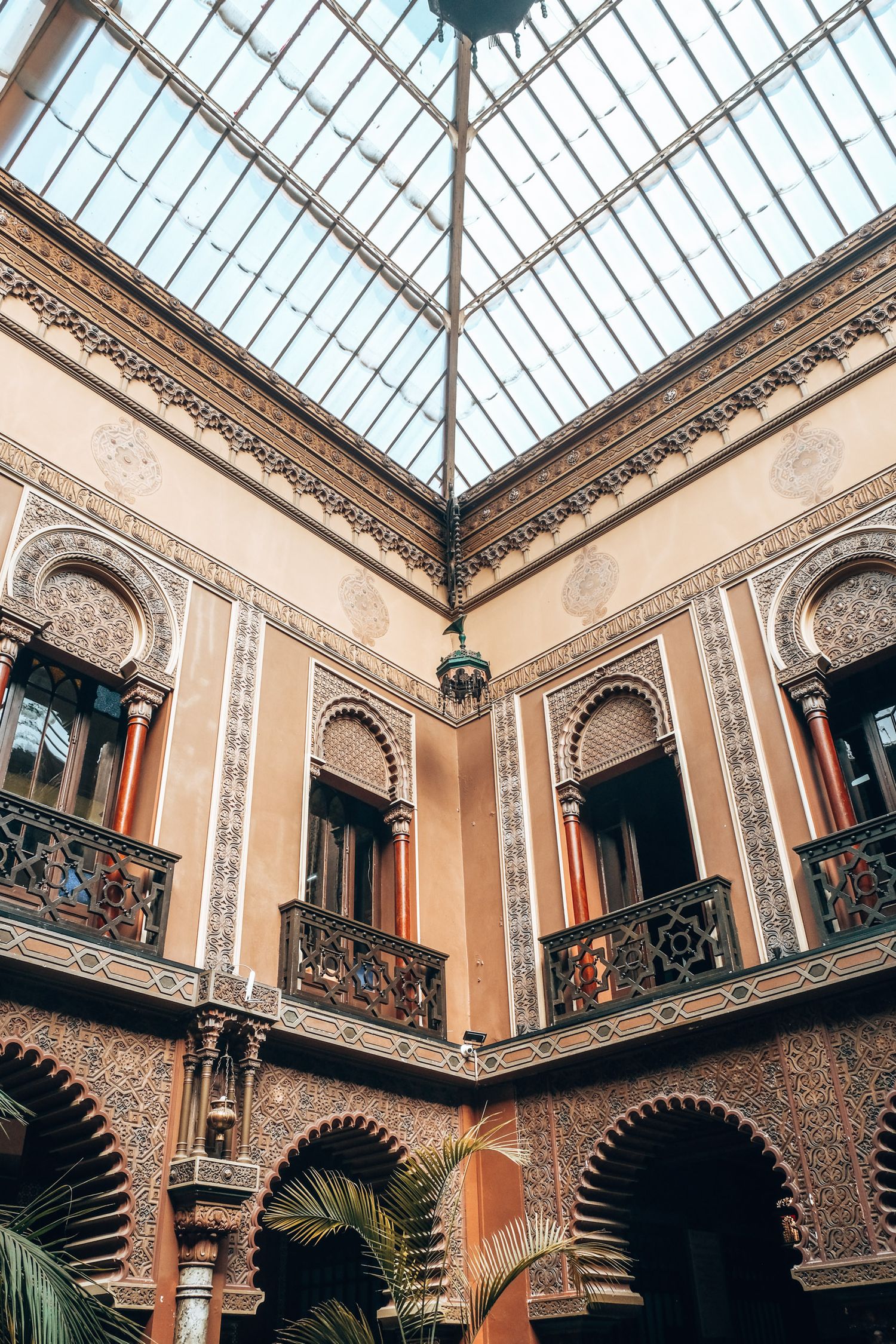 Ornate Moorish-style interior courtyard with arched balconies, intricate tilework, and a glass skylight ceiling.