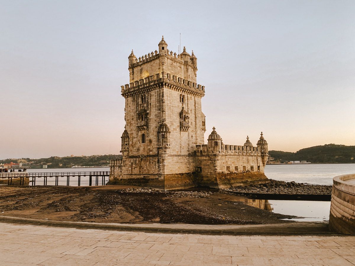 Historic Belem Tower standing on the Tagus River in Lisbon, Portugal, at golden hour with calm waters surrounding it.