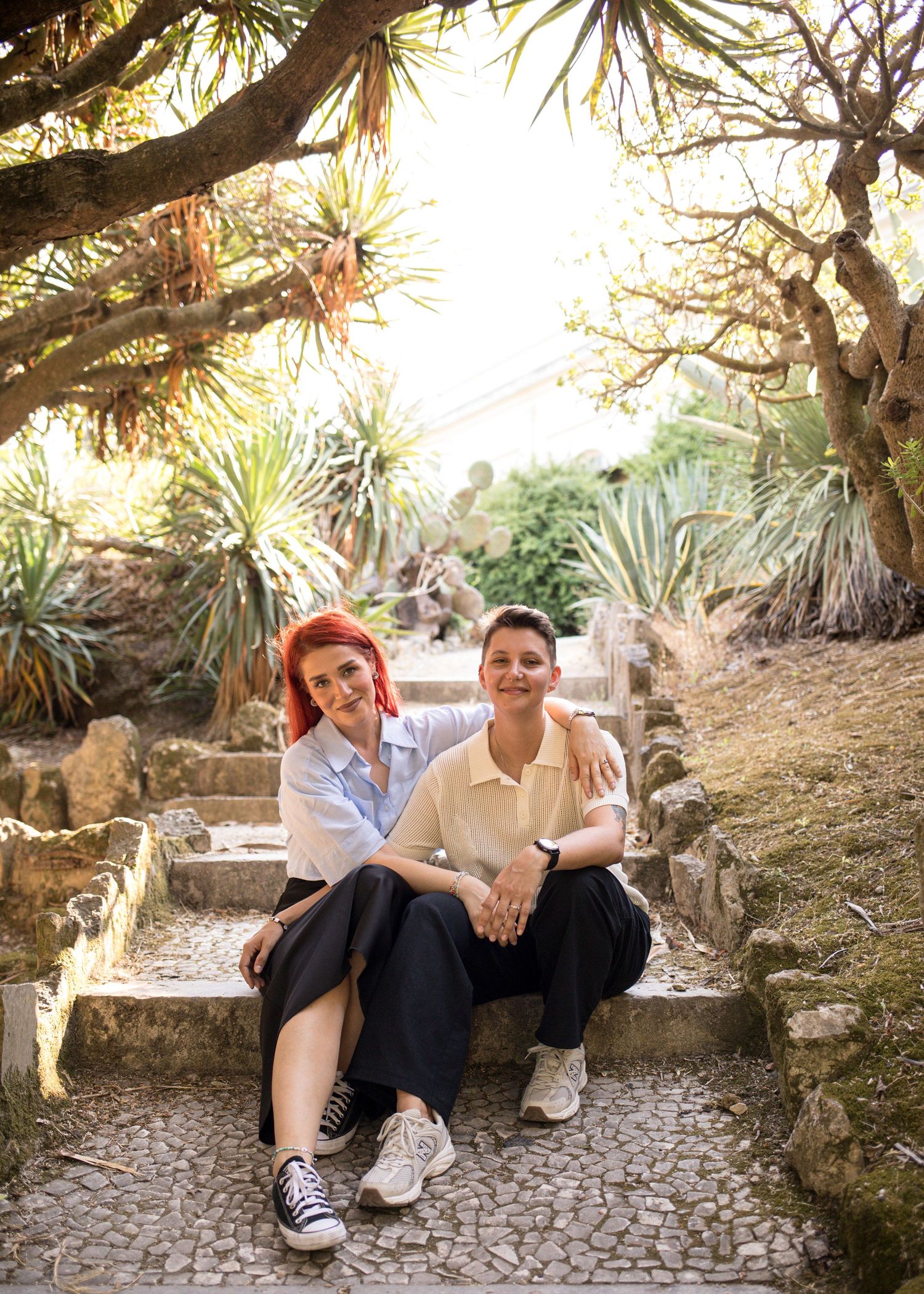 Couple sitting on garden steps during a relaxed photoshoot in Lisbon with palms and warm sunlight.