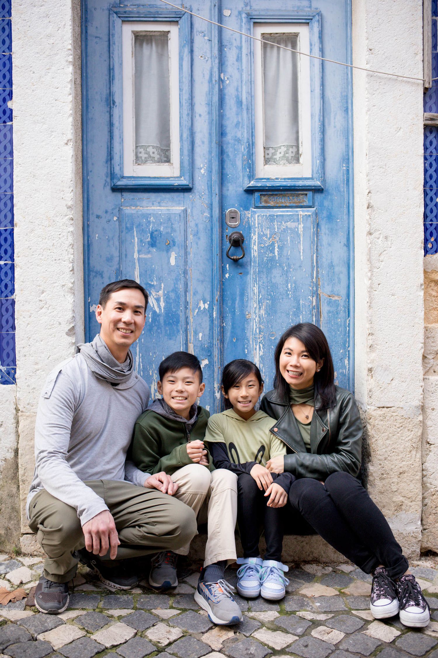 Family photoshoot in Lisbon with parents and two children smiling together in front of a weathered blue door.