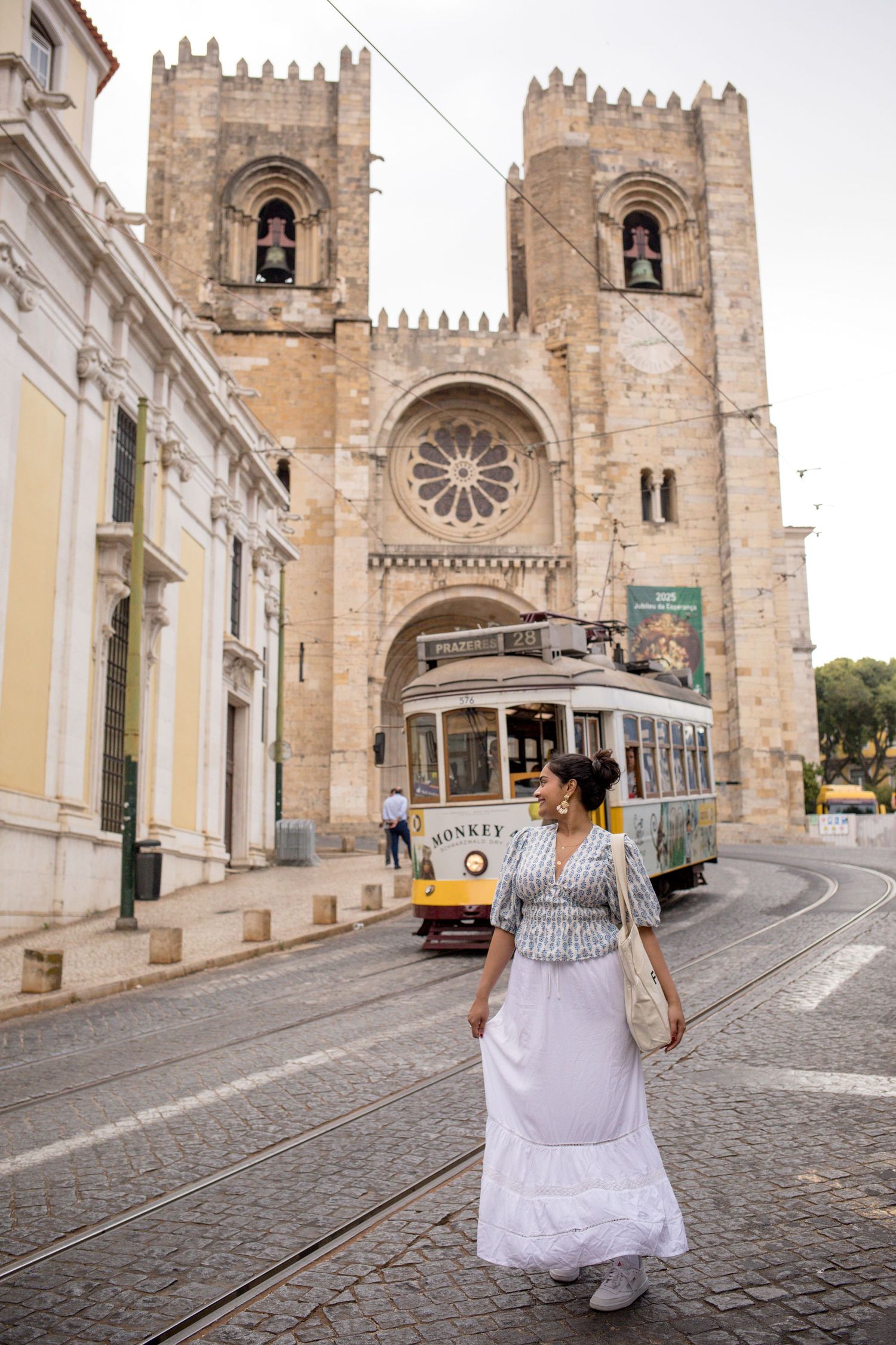 Solo traveller photoshoot in Lisbon with a woman by Tram 28 and Lisbon Cathedral on a cobbled street.