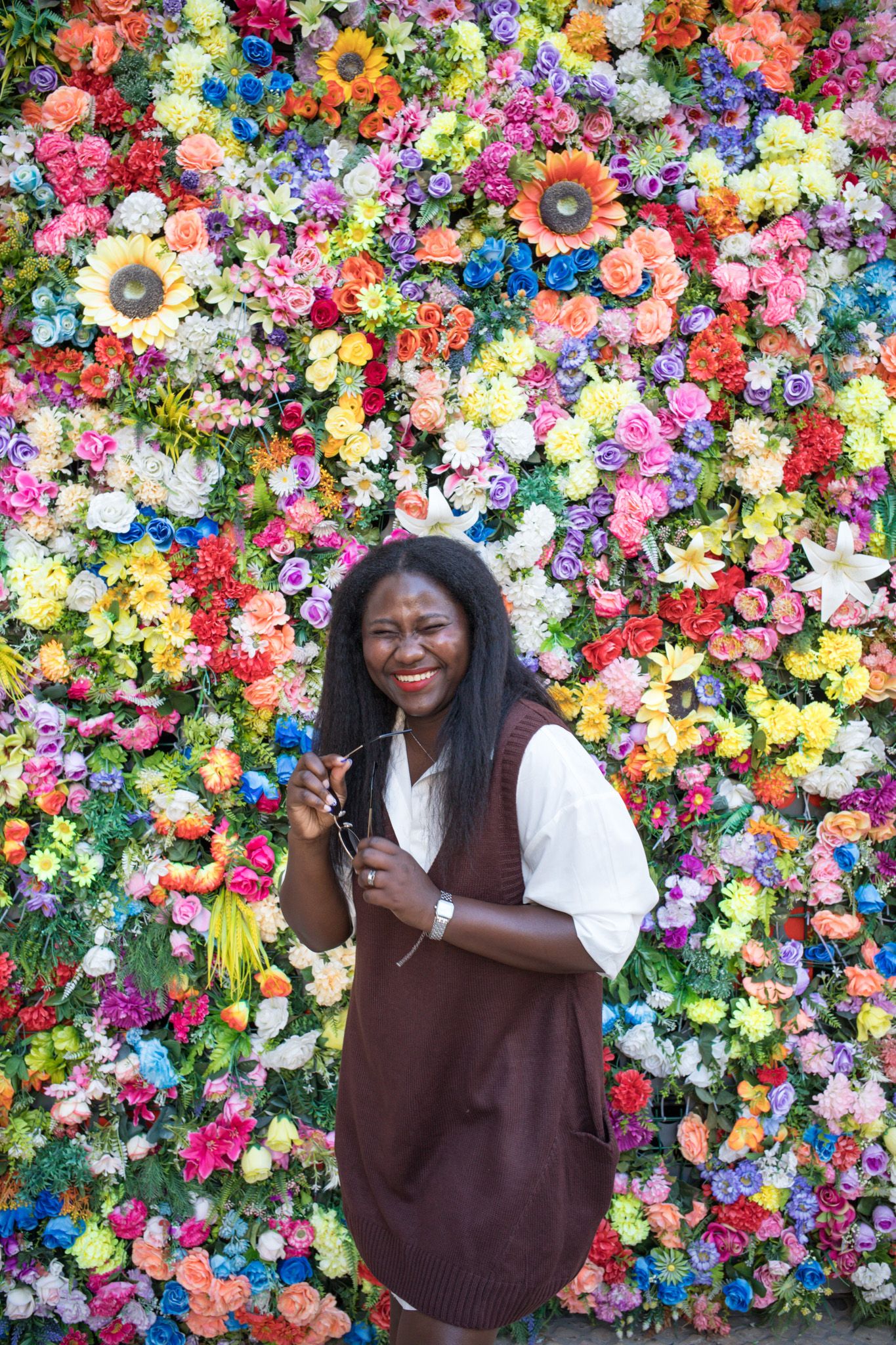 Smiling woman posing in front of vibrant colorful flower wall backdrop.