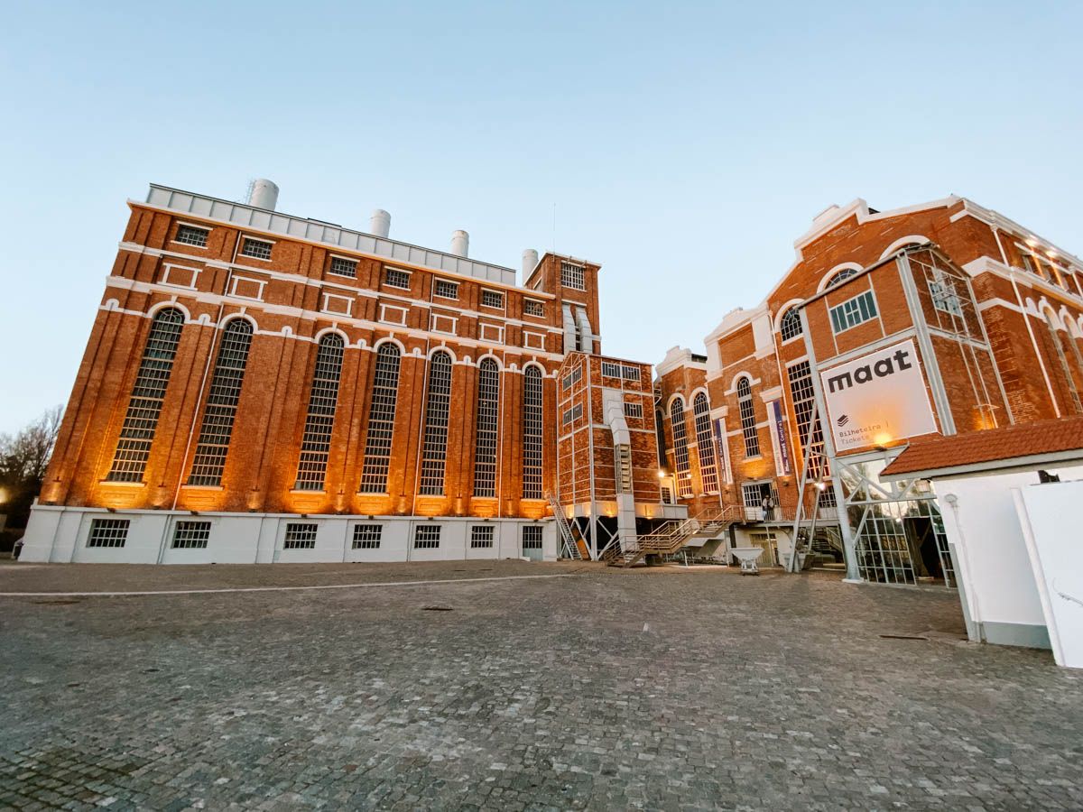 Illuminated historic red brick MAAT museum building exterior at dusk in Lisbon, Portugal.