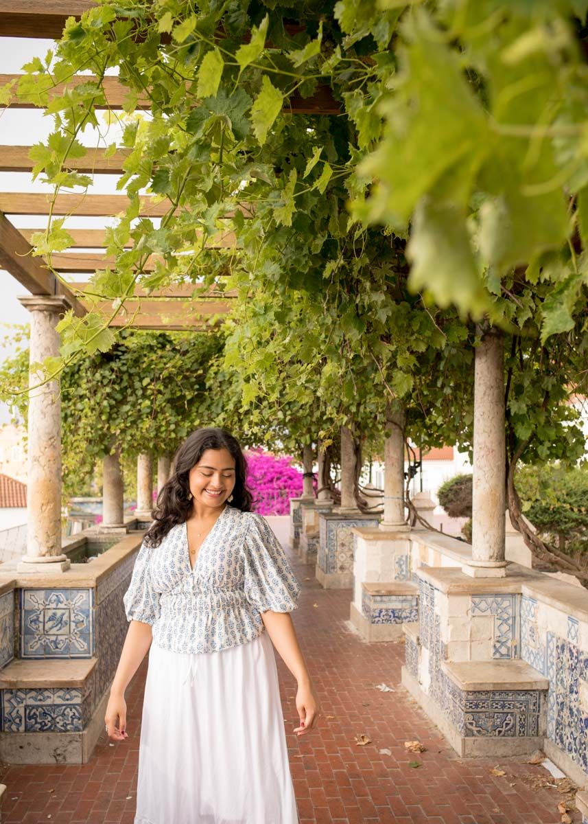 Woman smiling beneath leafy vines and blue tiled walls during a relaxed solo photoshoot in Lisbon.