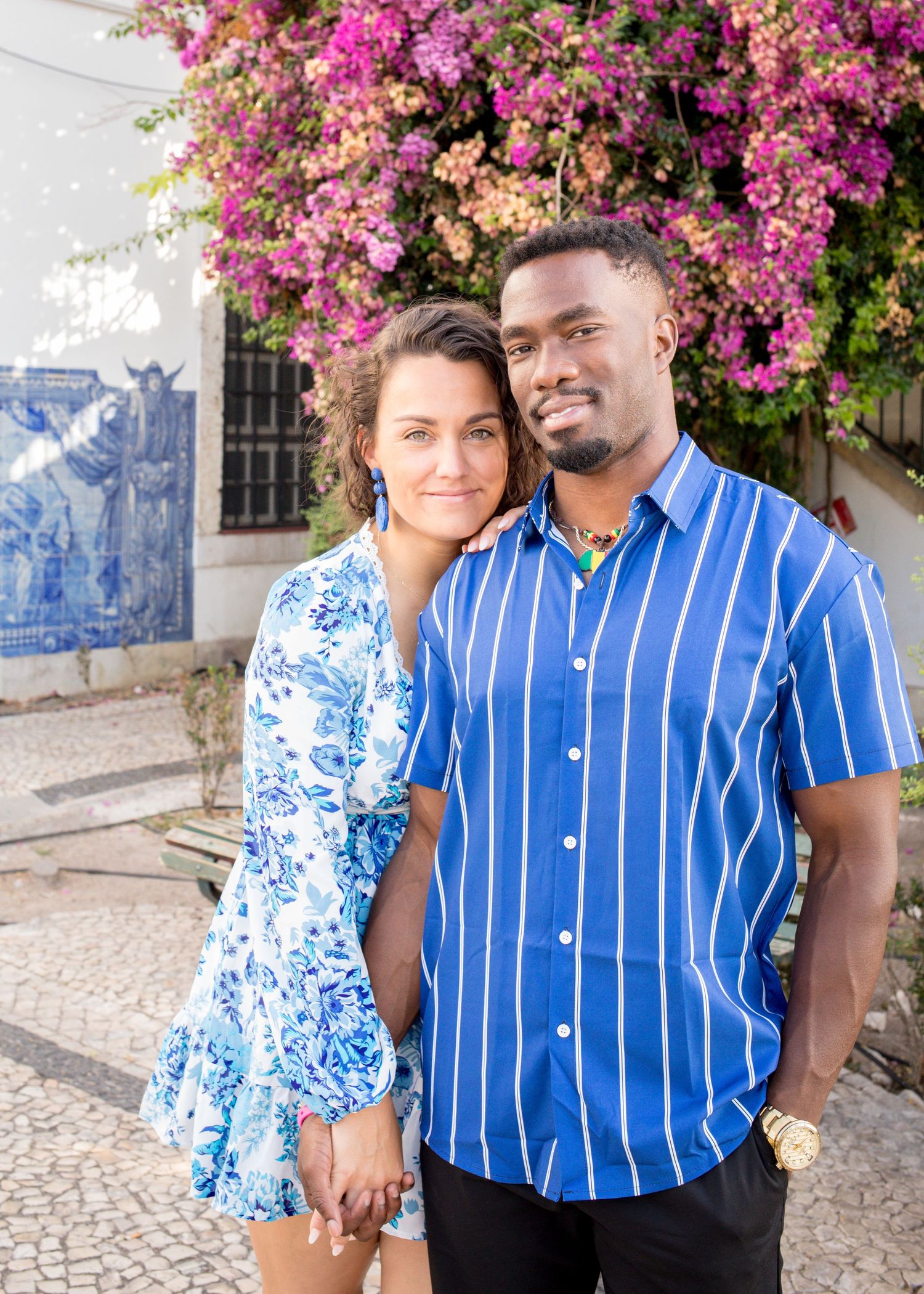 Couple poses together in front of colorful bougainvillea and traditional Portuguese blue tiles.