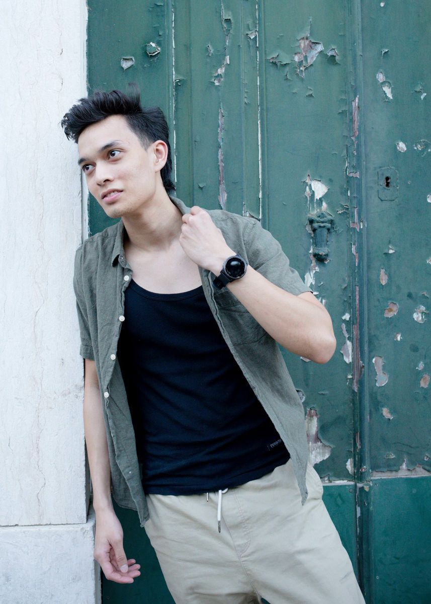 Stylish young man in gray shirt leaning against weathered green door outdoors.