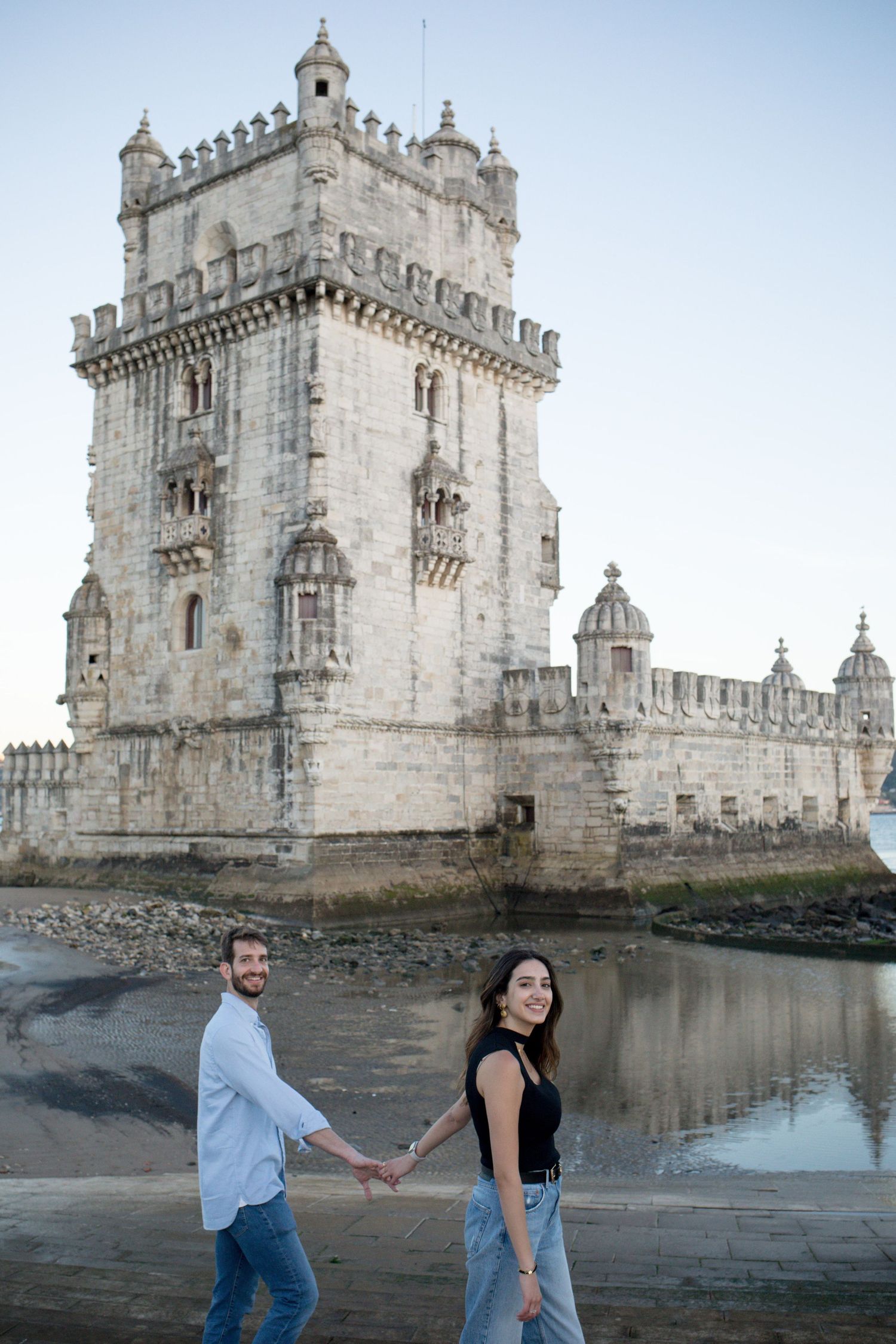 Couple holding hands in front of the historic Torre de Belem tower in Lisbon, Portugal.