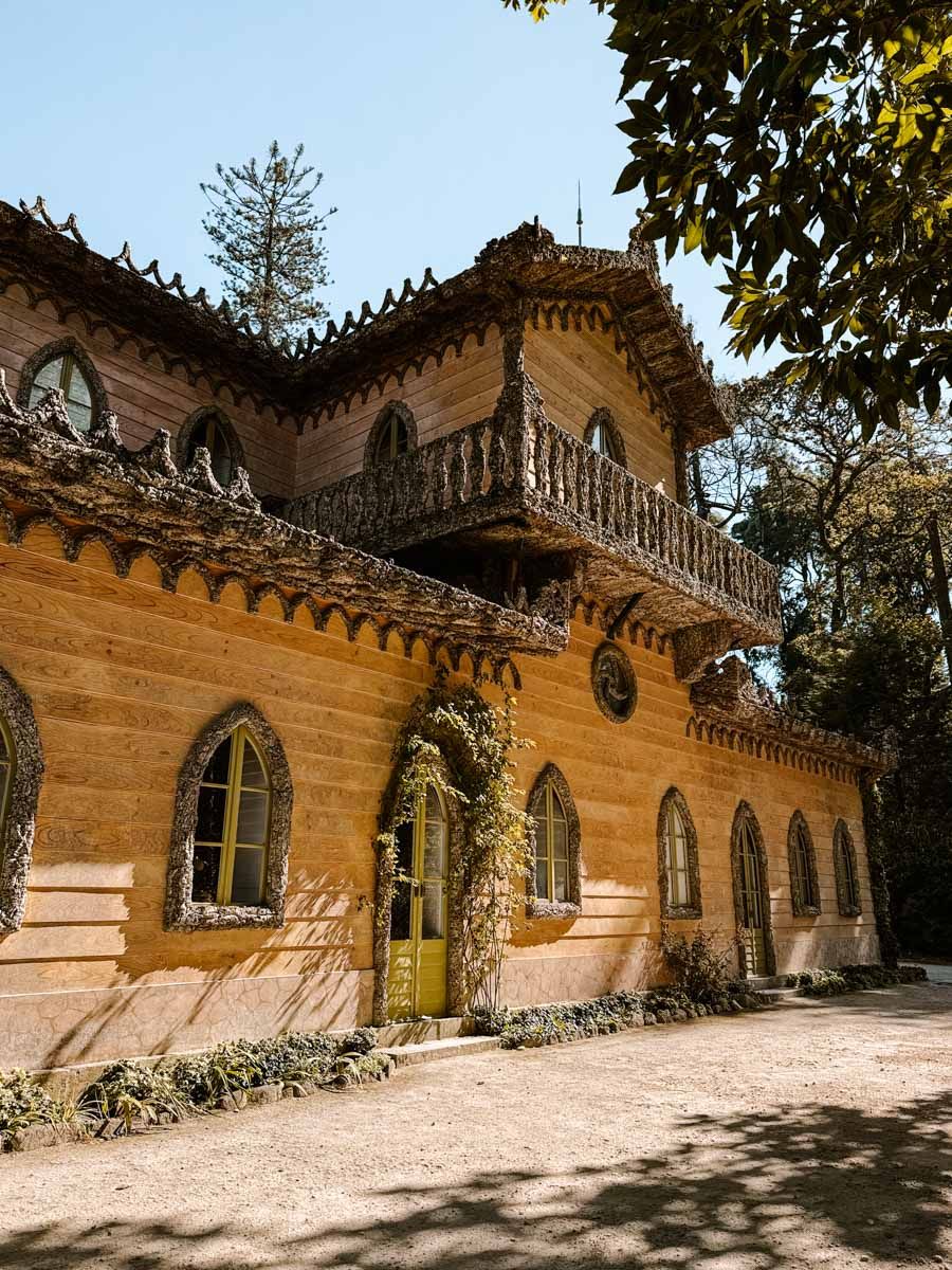 Ornate yellow building with Gothic arched windows, decorative trim, and ivy-covered walls surrounded by trees.