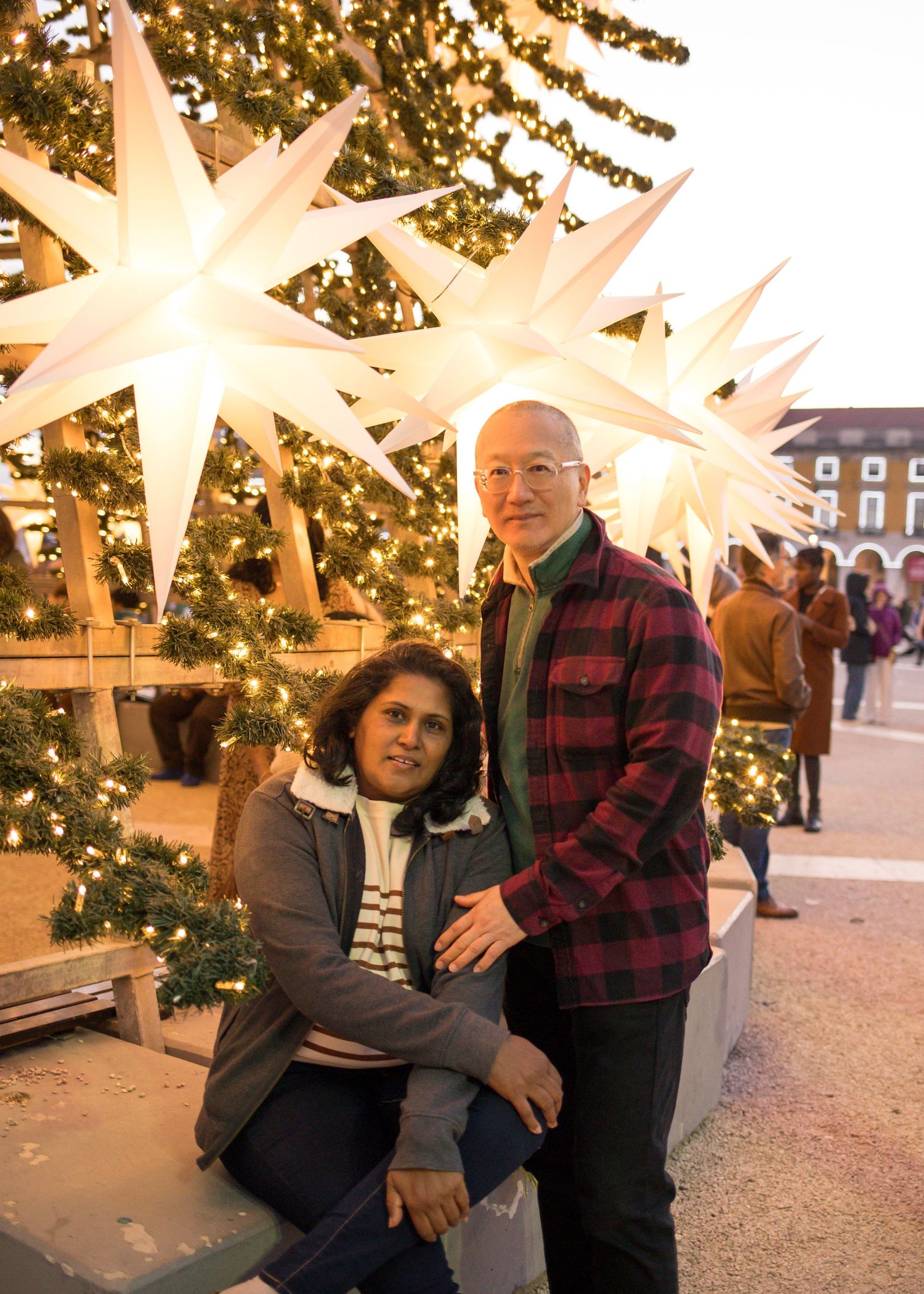 Couple posing together at an outdoor Christmas market with glowing star decorations and festive lights.