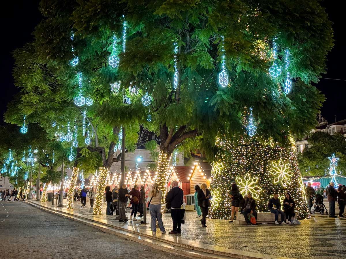 A large tree adorned with teal Christmas lights at a festive outdoor market at night.