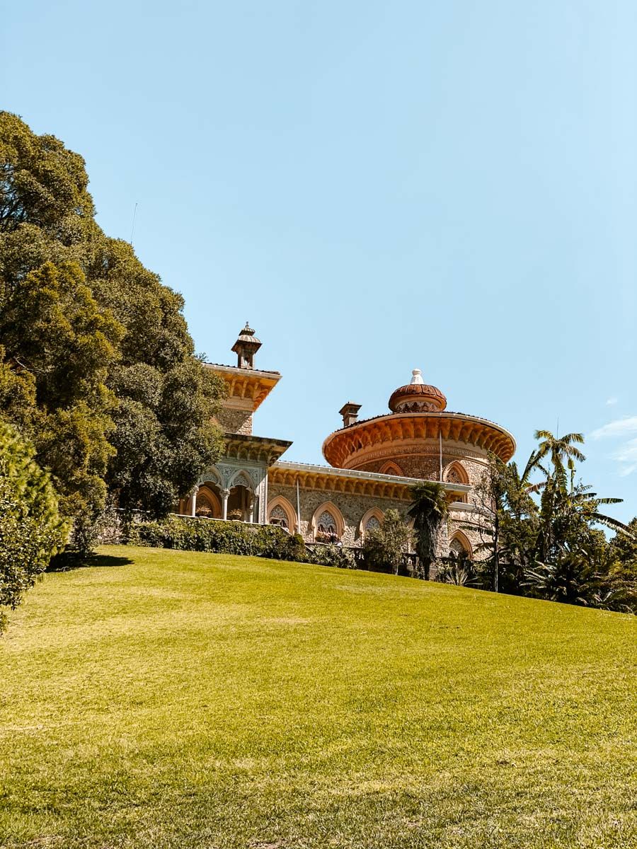 Ornate Moorish-style palace with arched colonnades and domed towers set on a lush green hillside under blue sky.