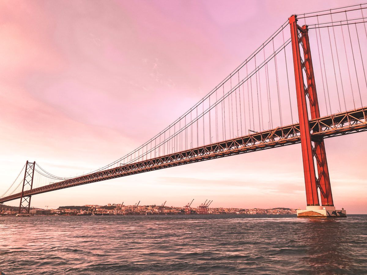 Red suspension bridge over calm waters at pink sunset, resembling San Francisco's Golden Gate Bridge.
