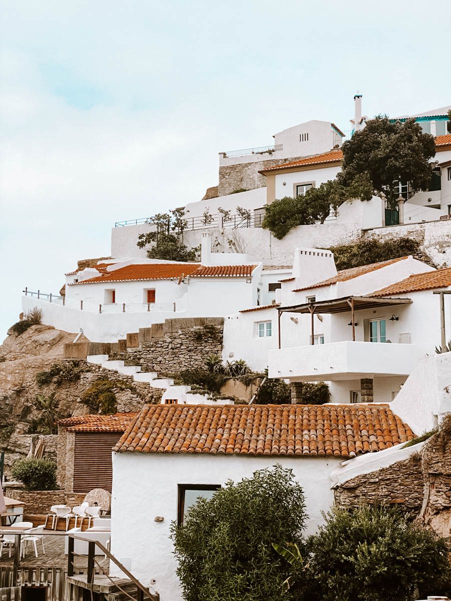 White-washed Mediterranean hillside village with terracotta rooftops and lush greenery under a soft cloudy sky.
