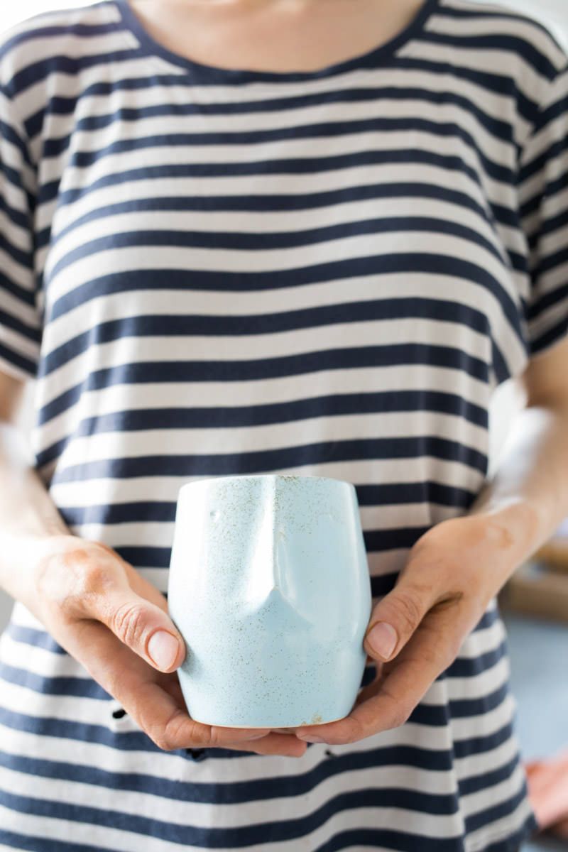 Woman in striped shirt holding a light blue ceramic cup with both hands.