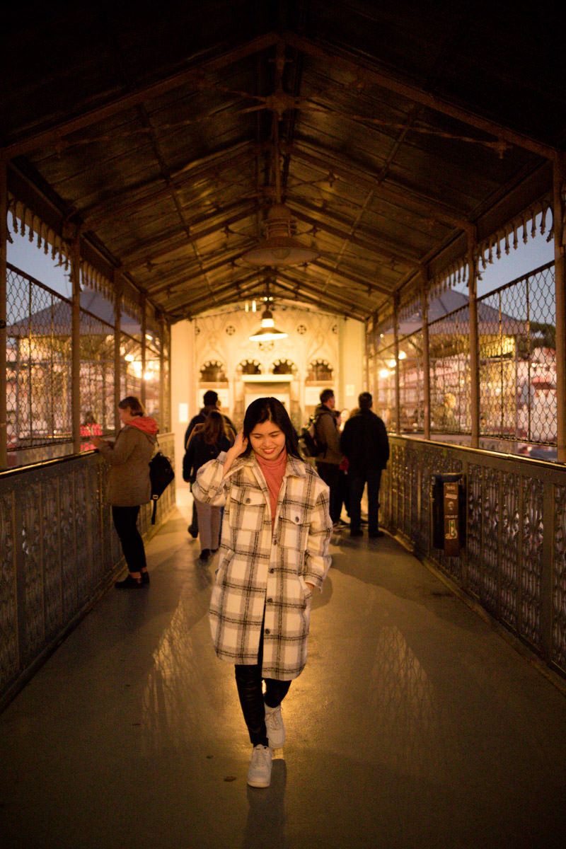 Woman in plaid coat smiling inside an ornate illuminated covered walkway at a temple at night.