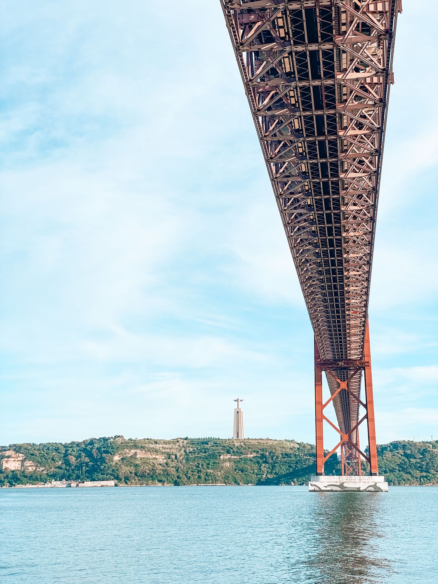 View from below the 25 de Abril Bridge in Lisbon, Portugal, with the Cristo Rei statue visible in the background.