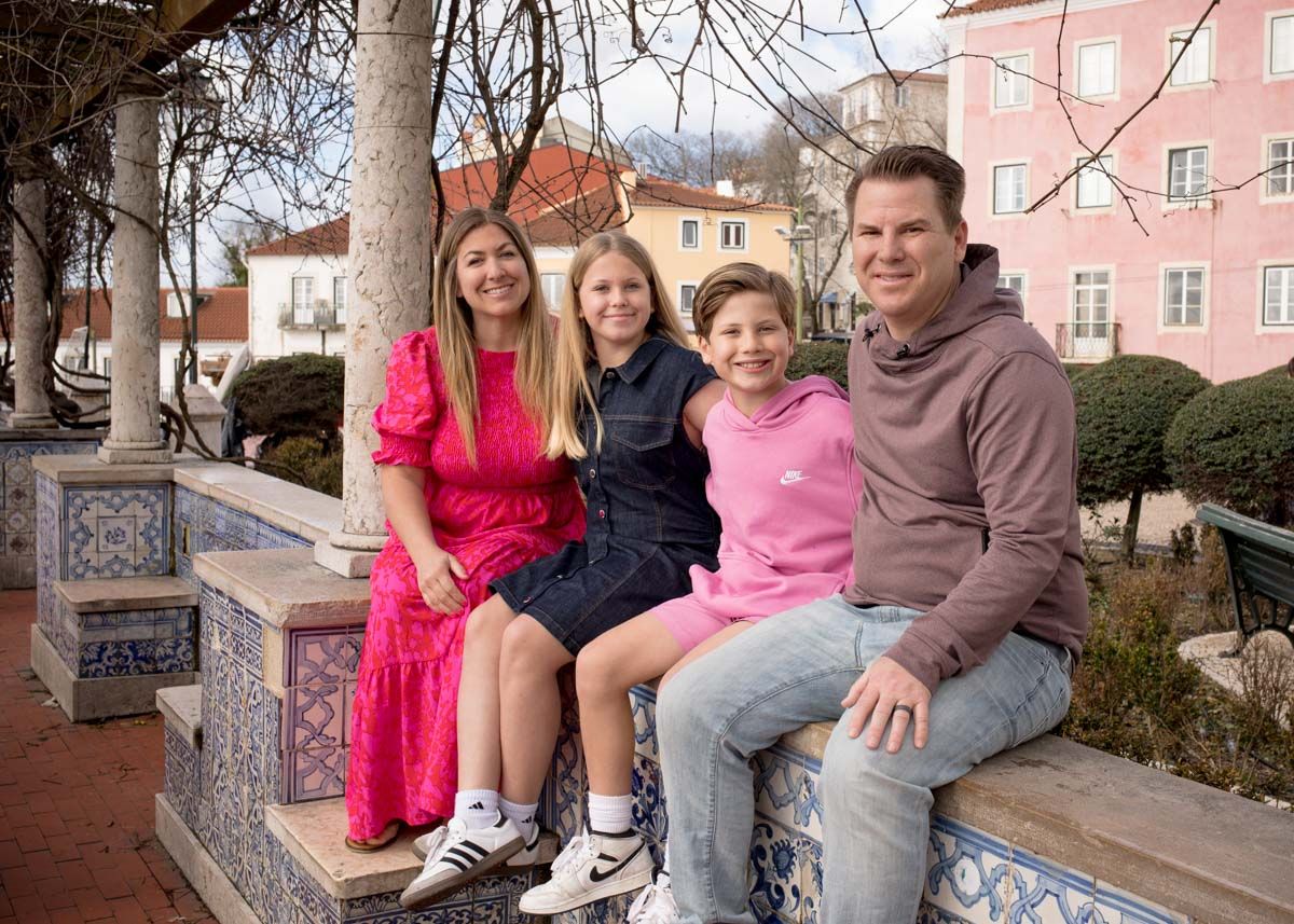 Happy family of four sits on ornate tiled bench in Sintra, Portugal, with colorful buildings in the background.