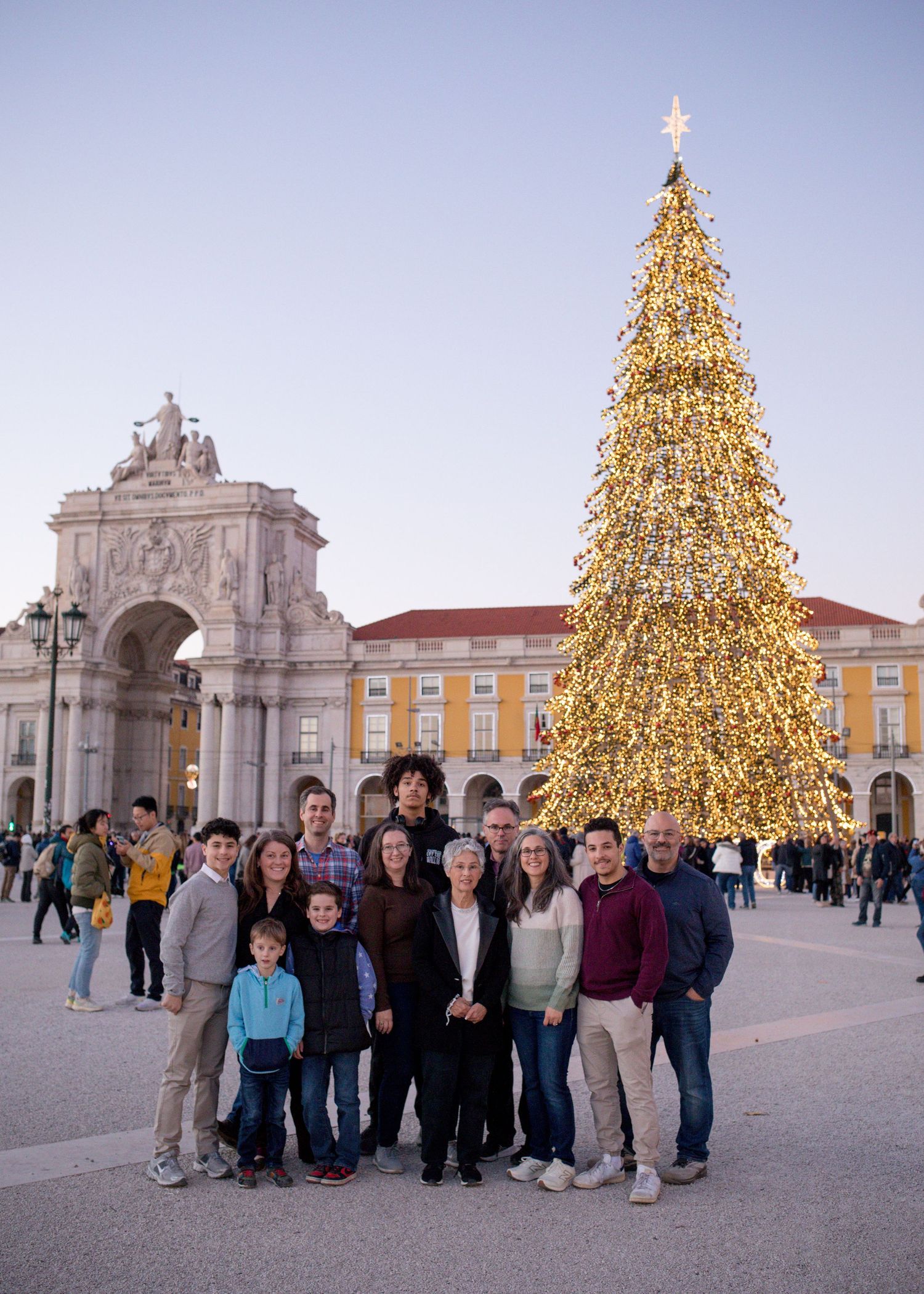 Family group posing in front of a large Christmas tree at Lisbon's Praca do Comercio with the Rua Augusta Arch.