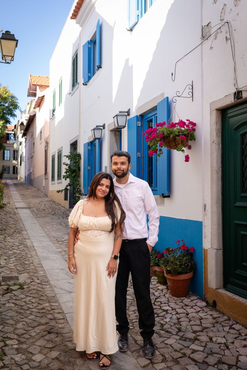 Couple posing on a charming cobblestone street with white buildings and blue shutters in Portugal.
