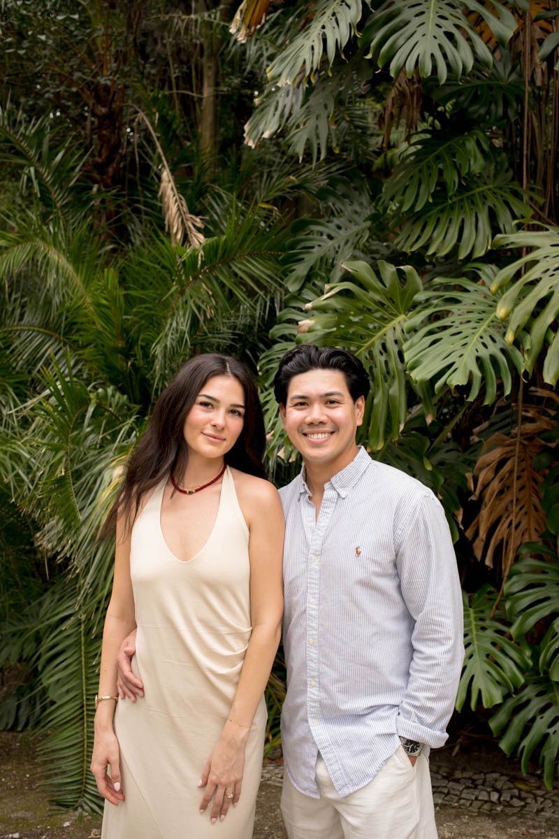 Smiling couple posing together in front of lush tropical greenery and monstera leaves.