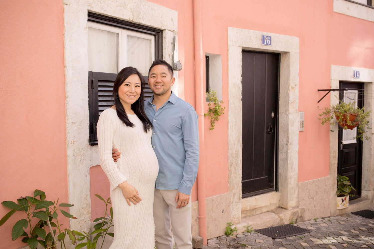 Pregnant woman and partner posing in front of a charming pink building on a Lisbon street.