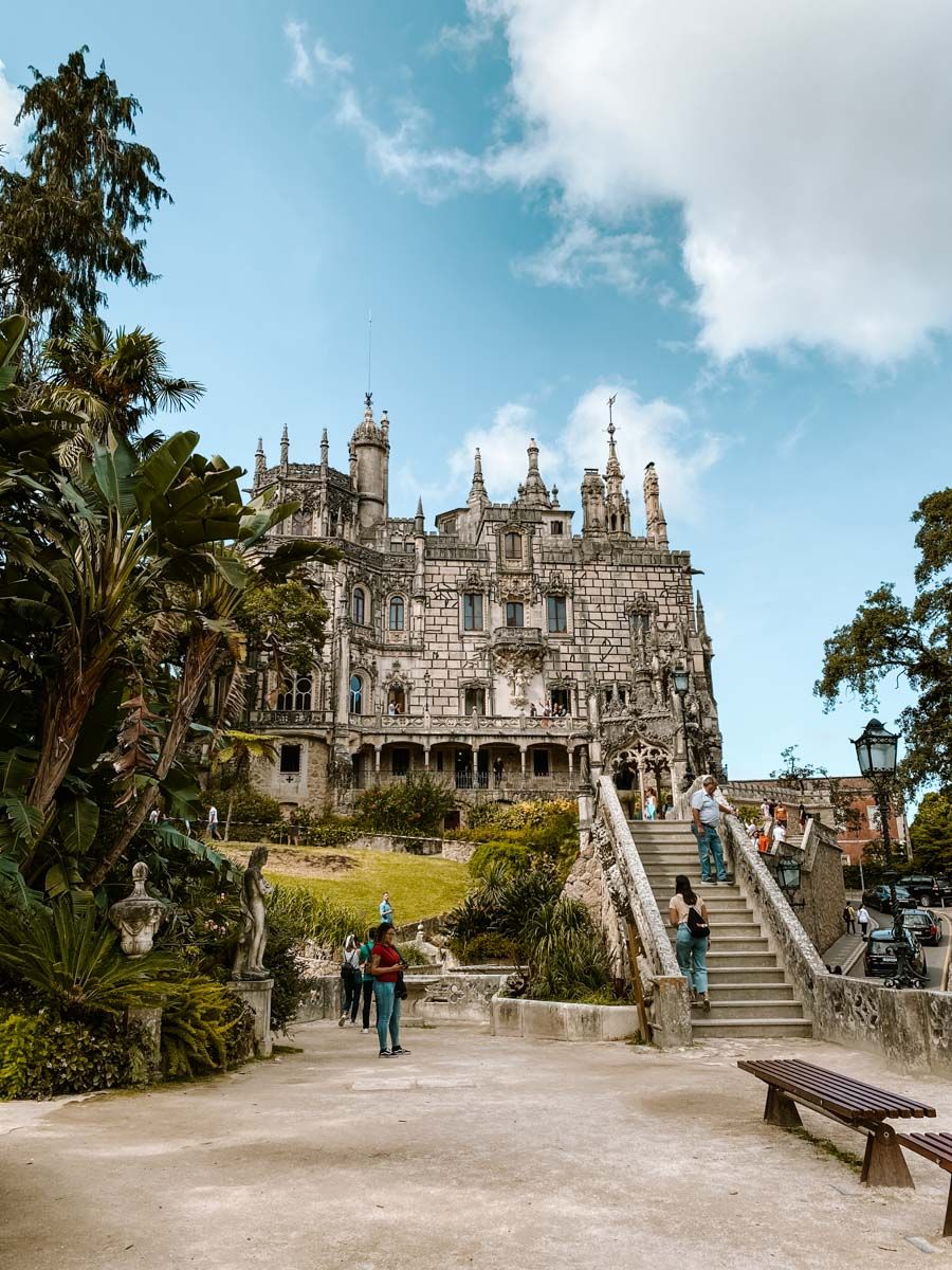 Gothic Quinta da Regaleira palace with lush gardens and stone staircase under blue sky in Sintra, Portugal.