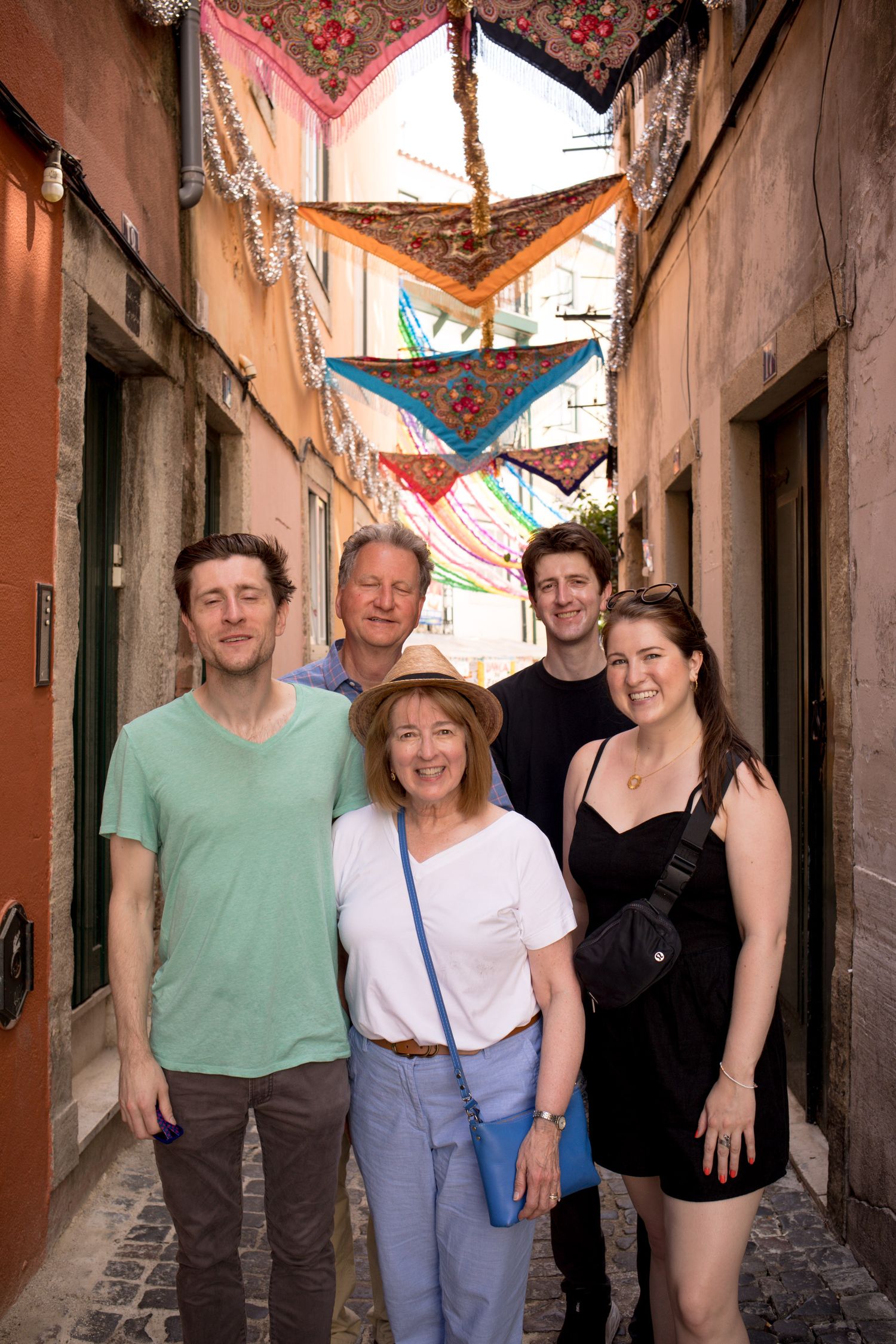 Family of five posing in a colorful narrow alley decorated with hanging scarves in Lisbon, Portugal.
