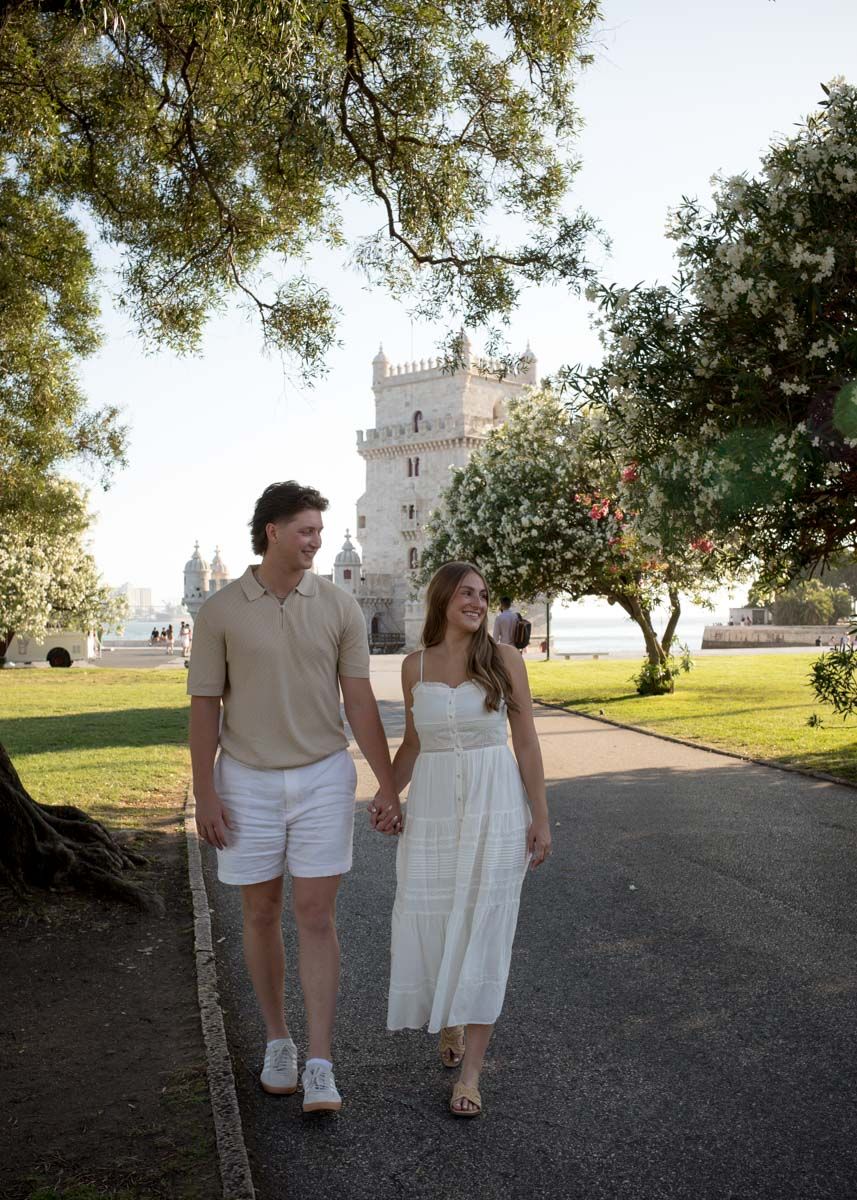 Couple holding hands walking near Belem Tower in Lisbon, Portugal on a sunny day.