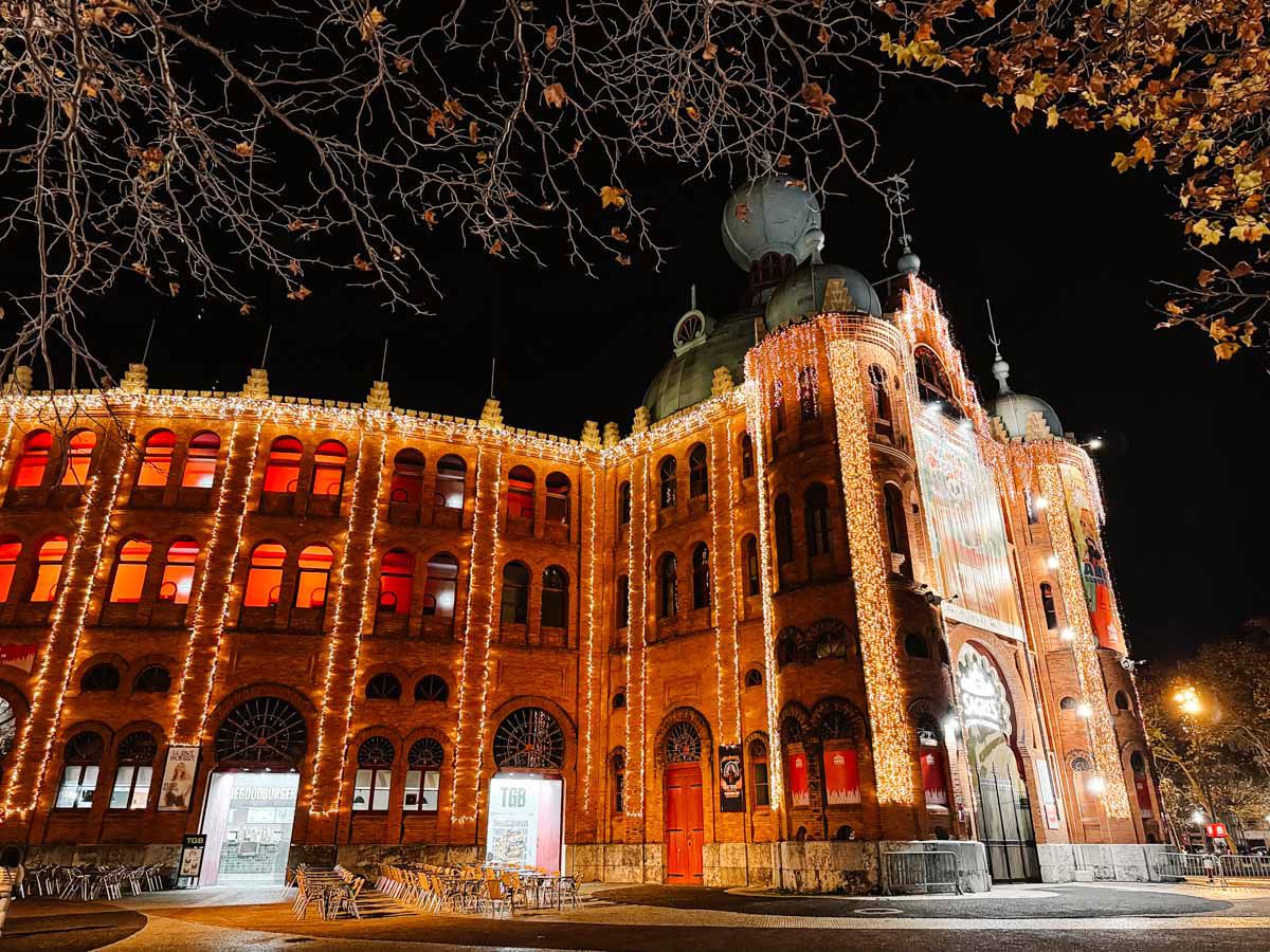 Historic bullring building illuminated with festive red Christmas lights at night, ornate Moorish Revival architecture glowing dramatically.